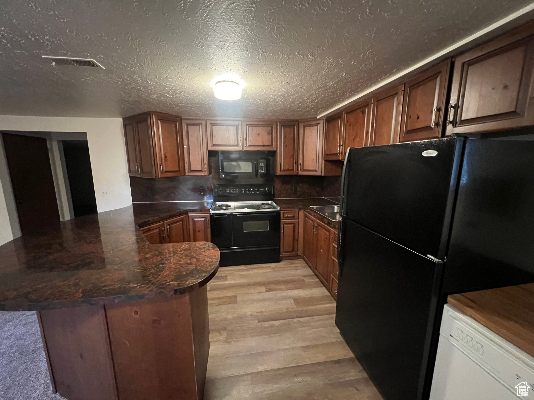 Kitchen with kitchen peninsula, black appliances, a textured ceiling, and light hardwood / wood-style floors