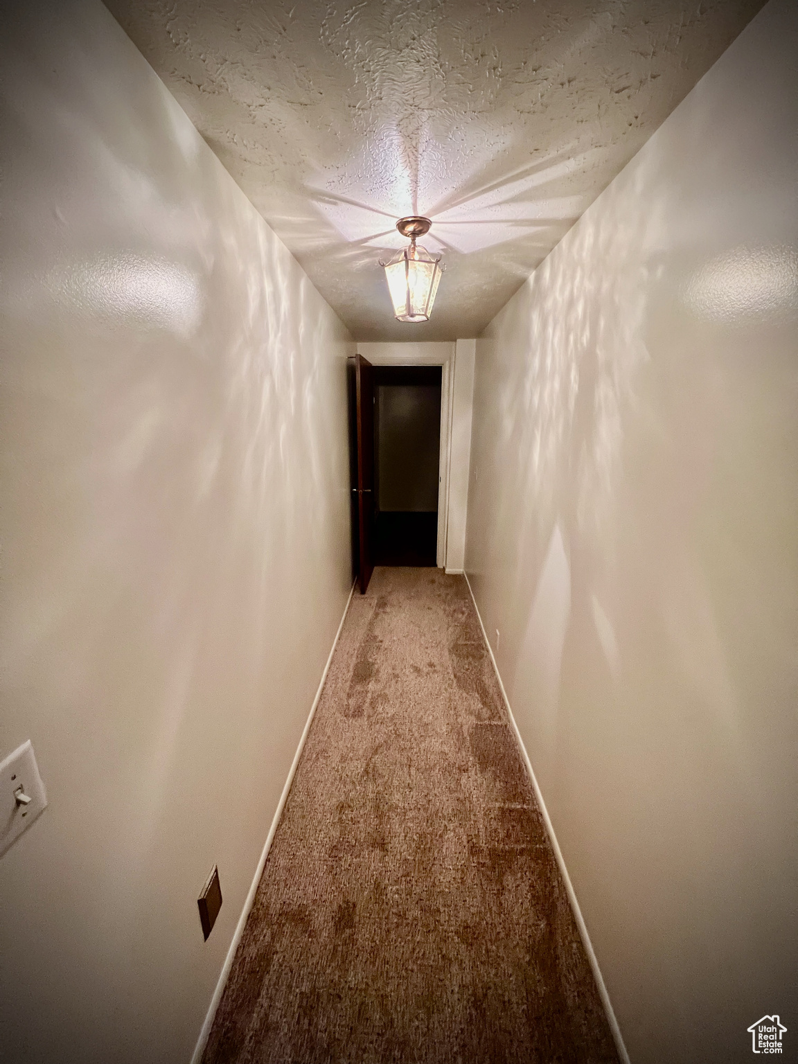 Corridor featuring light colored carpet and a textured ceiling