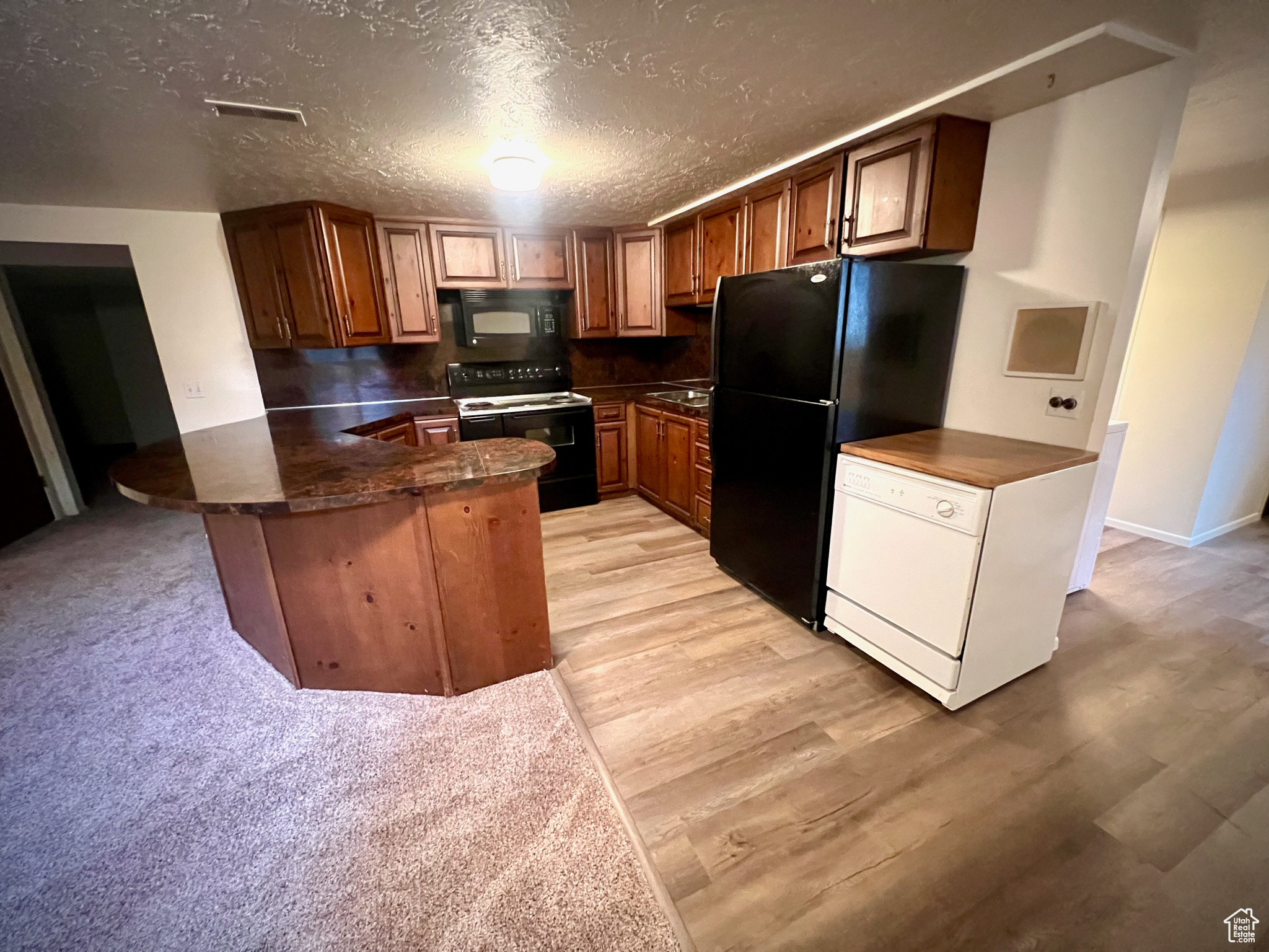 Kitchen with kitchen peninsula, light wood-type flooring, a textured ceiling, sink, and black appliances