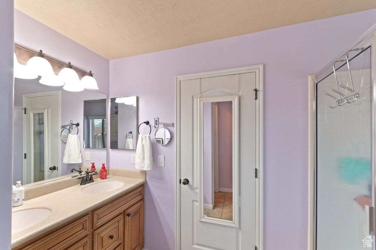 Bathroom featuring a shower with shower door, vanity with extensive cabinet space, and double sink