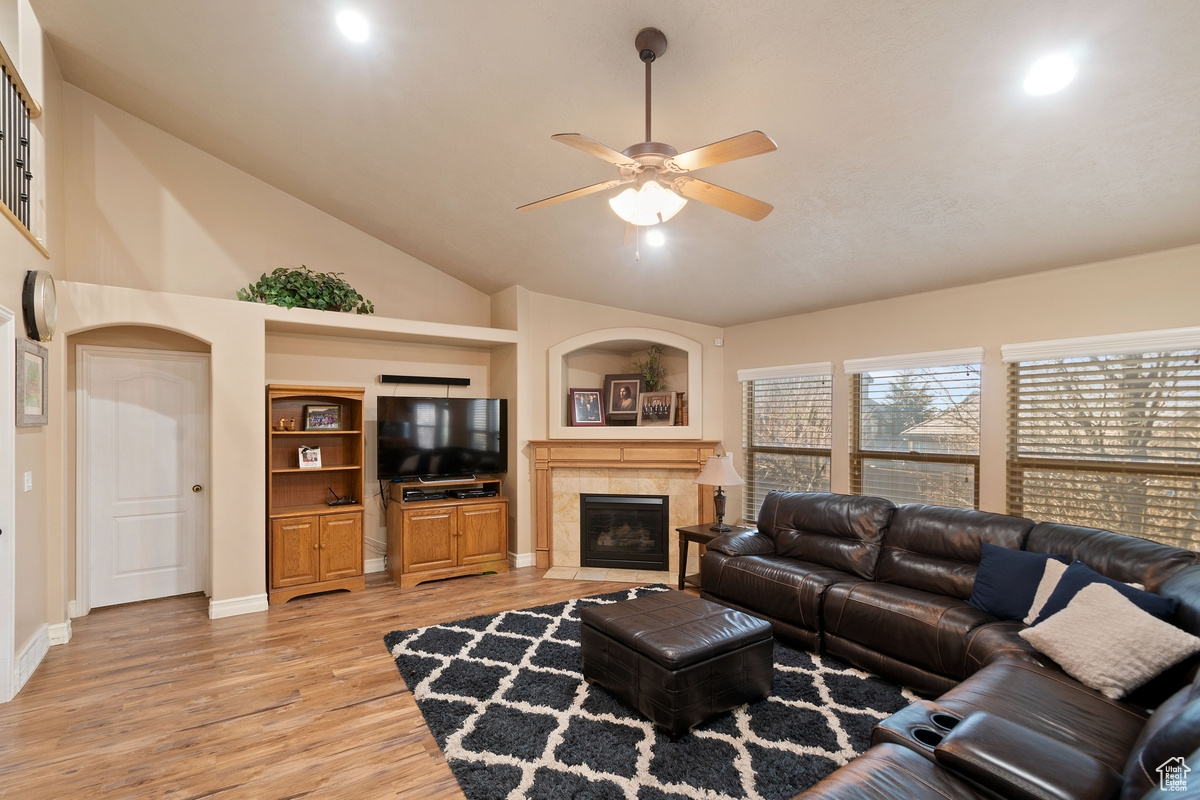 Living room featuring high vaulted ceiling, light wood-type flooring, a tile fireplace, and ceiling fan