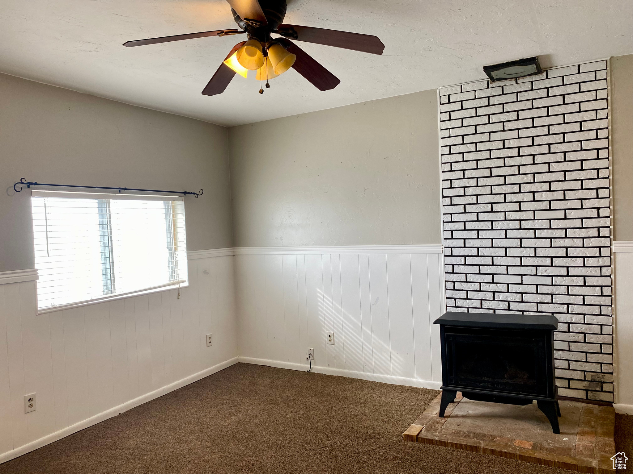 Interior space featuring brick wall, a brick fireplace, dark carpet, and ceiling fan