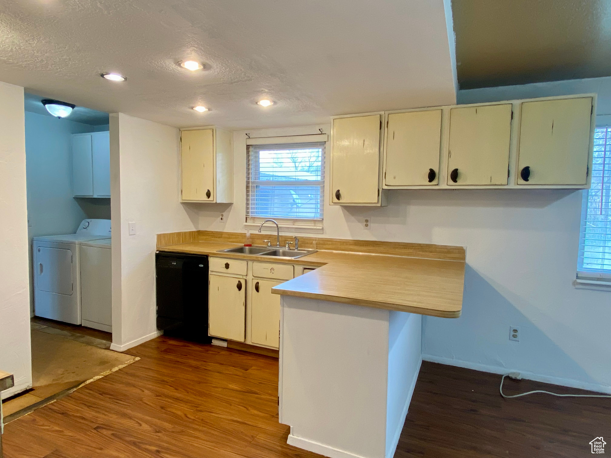 Kitchen with dark wood-type flooring, washer and clothes dryer, black dishwasher, and sink