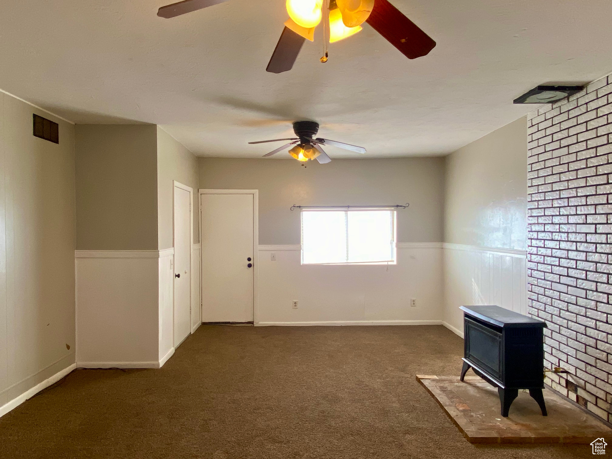 Spare room with brick wall, dark colored carpet, and ceiling fan