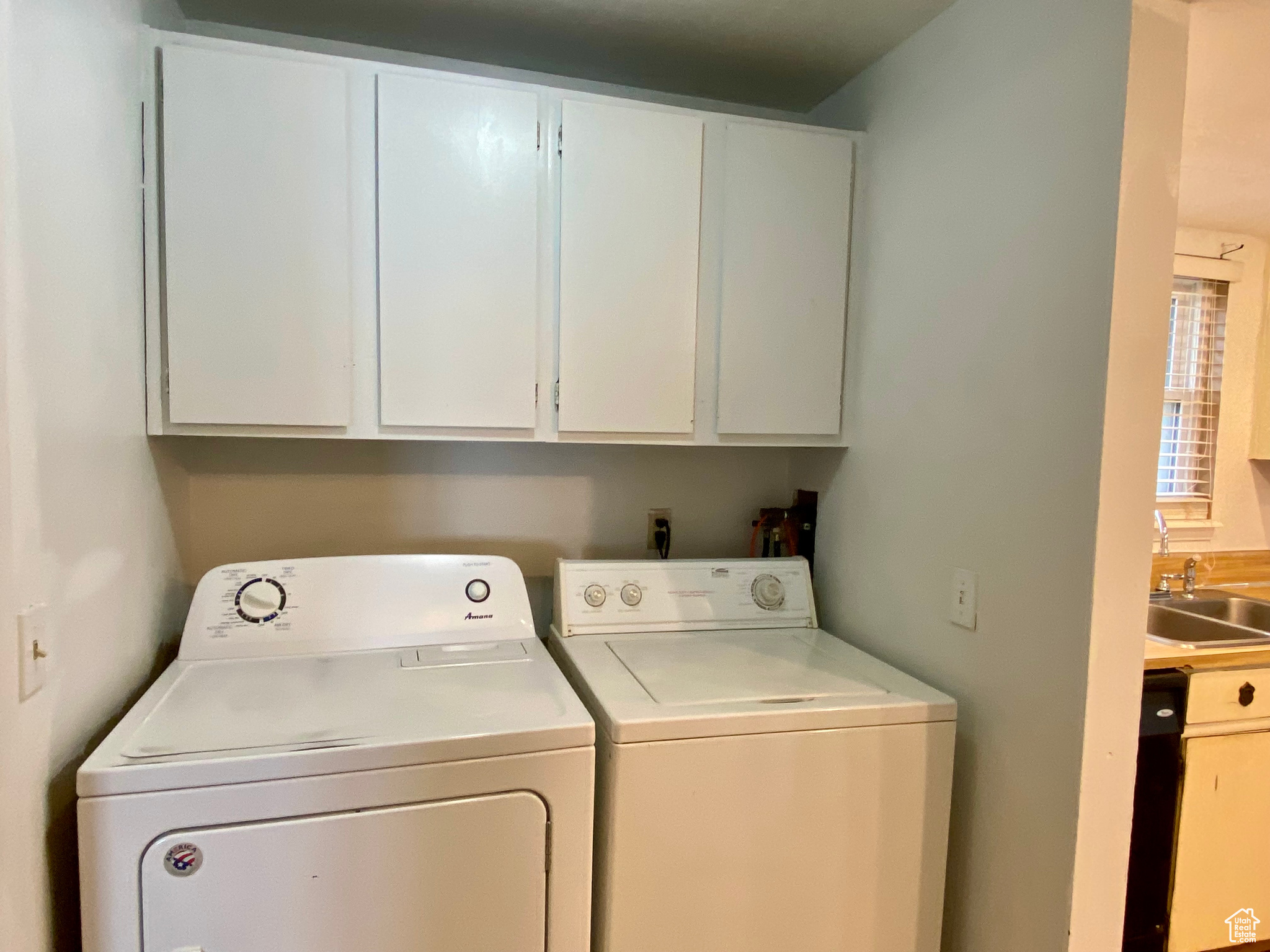 Clothes washing area with cabinets, washer and clothes dryer, and sink