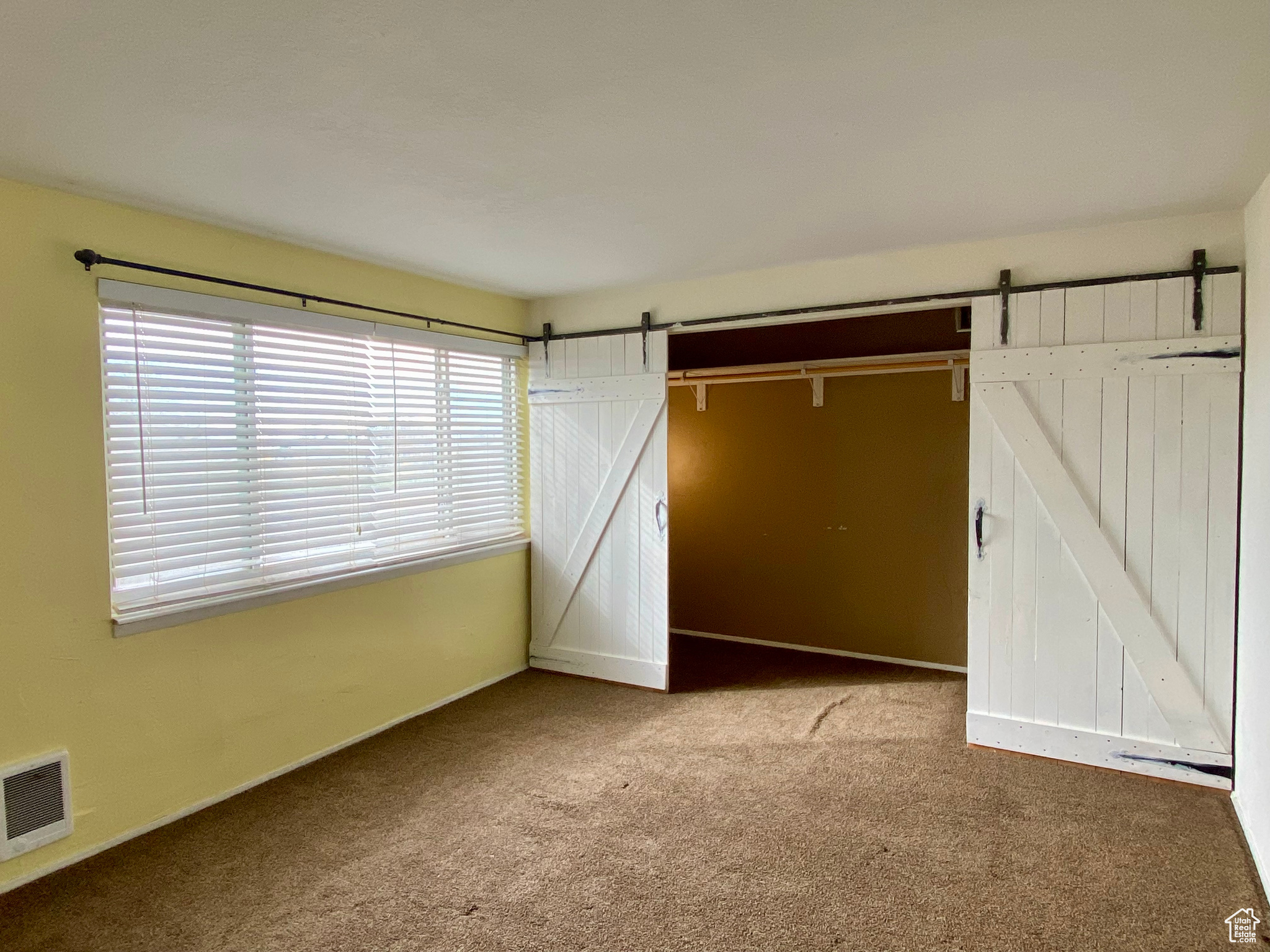 Unfurnished bedroom with a barn door and light colored carpet