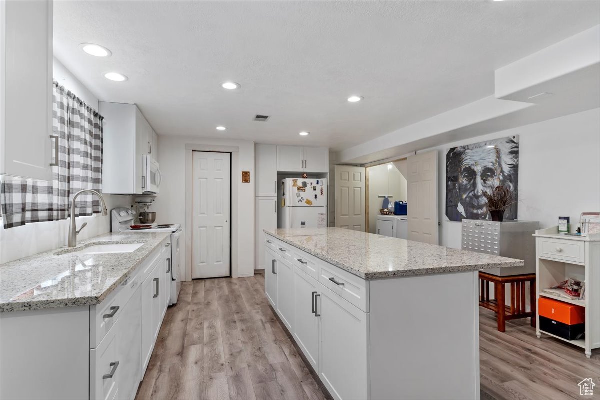 Kitchen with light stone counters, white appliances, white cabinetry, light hardwood / wood-style flooring, and a center island