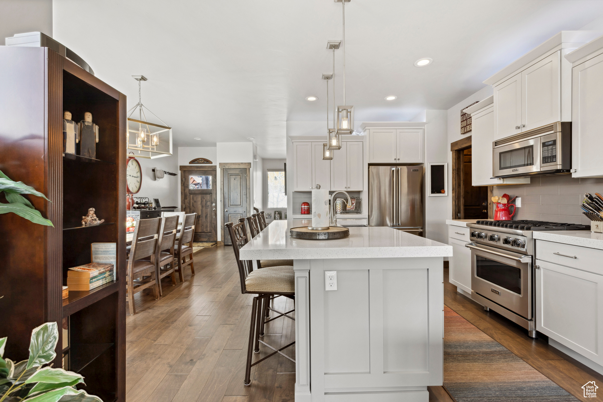 Kitchen with white cabinets, a kitchen island with sink, premium appliances, dark hardwood / wood-style flooring, and decorative light fixtures