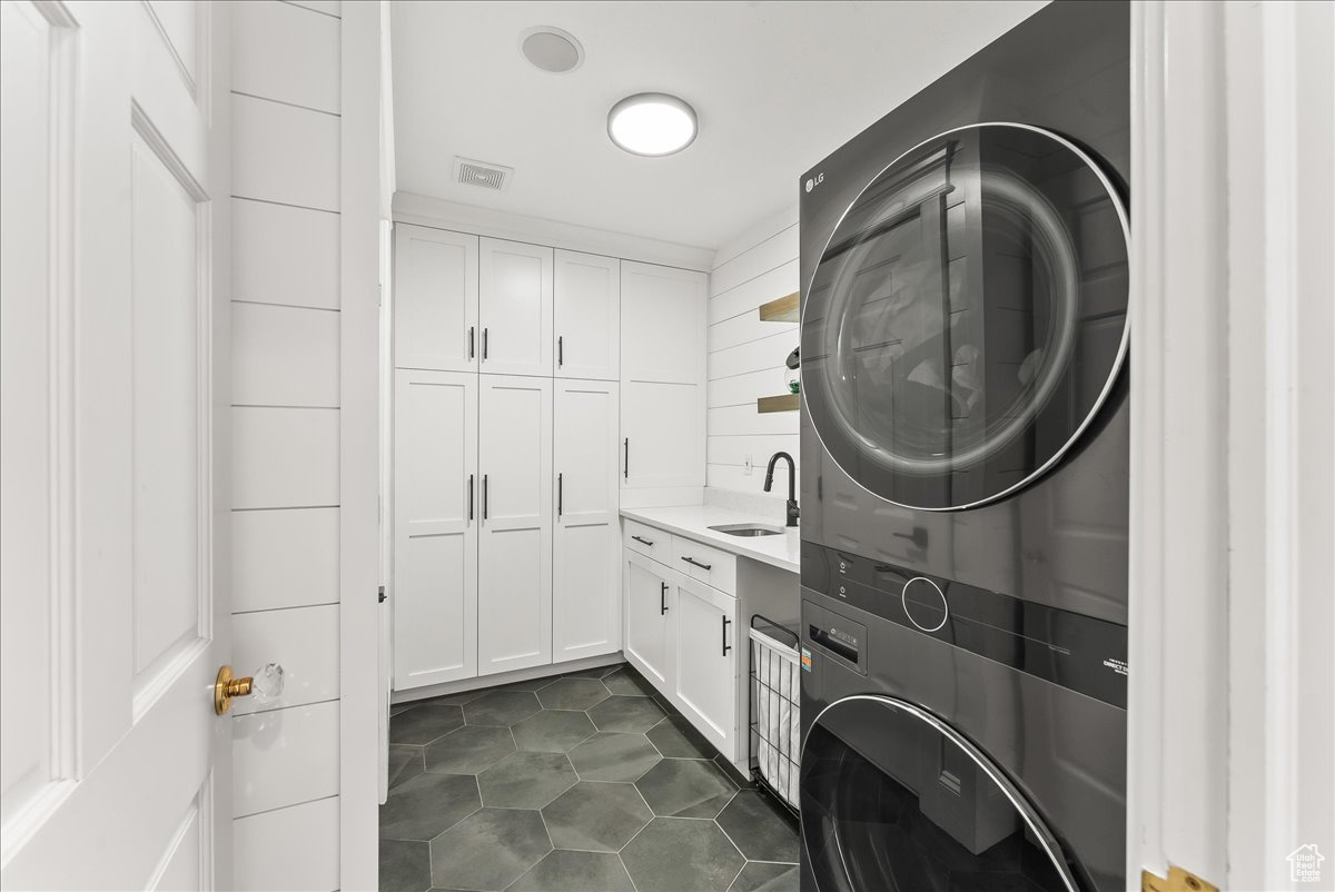 Laundry area featuring stacked washer / drying machine, cabinets, sink, and dark tile floors