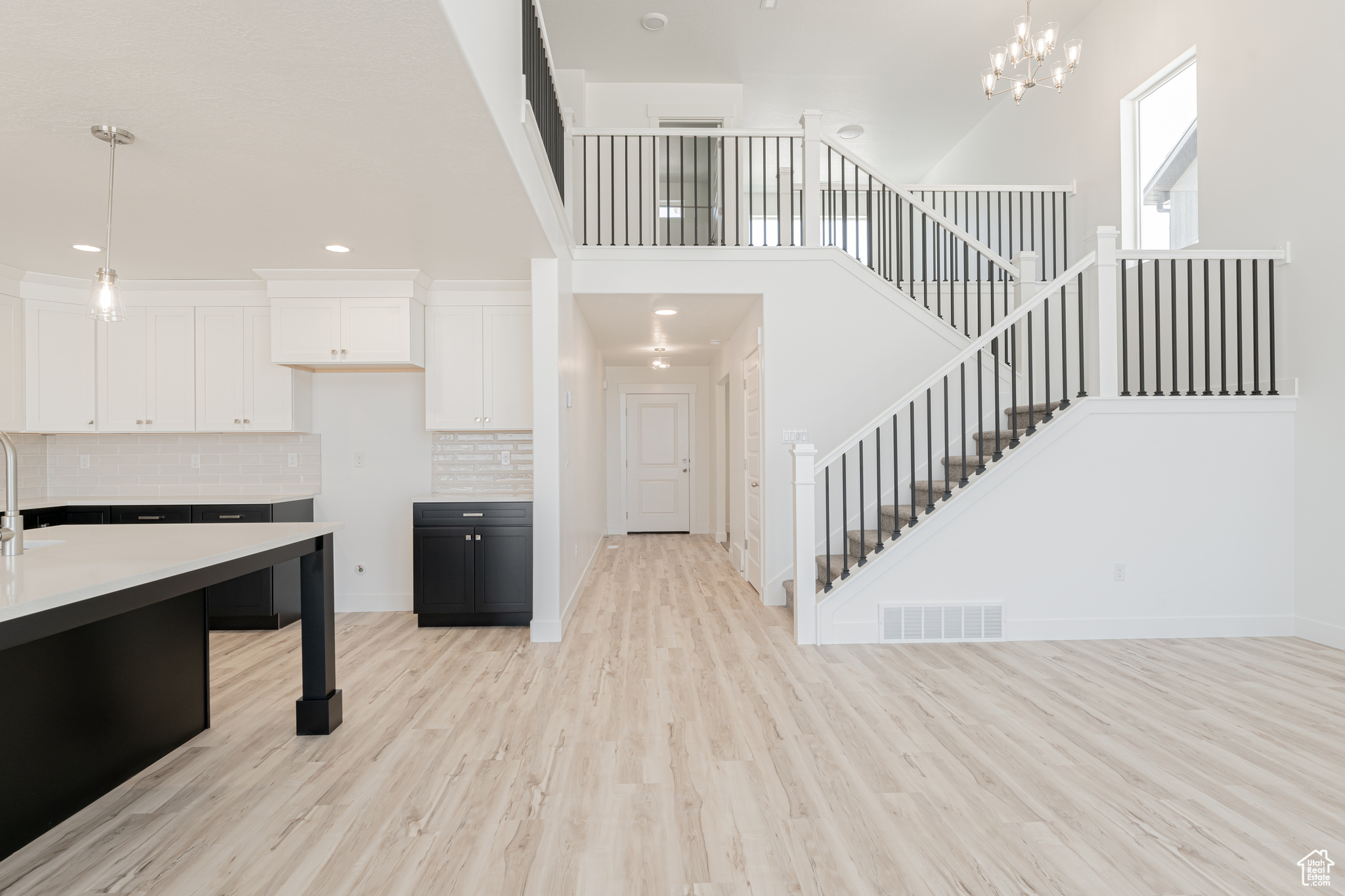 Kitchen with hanging light fixtures, white cabinets, light wood-type flooring, decorative backsplash, and a towering ceiling