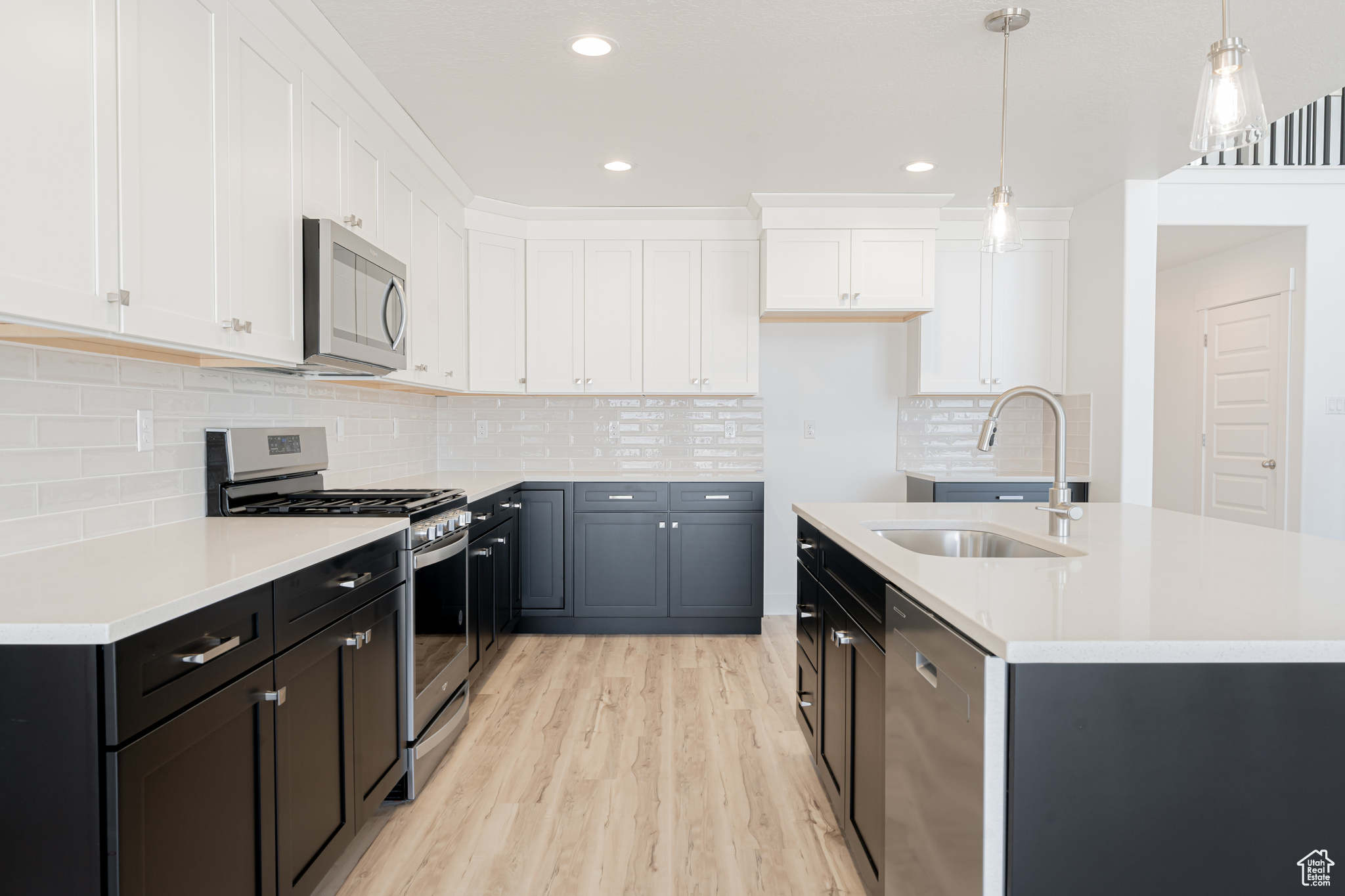 Kitchen featuring white cabinetry, backsplash, stainless steel appliances, light hardwood / wood-style floors, and sink