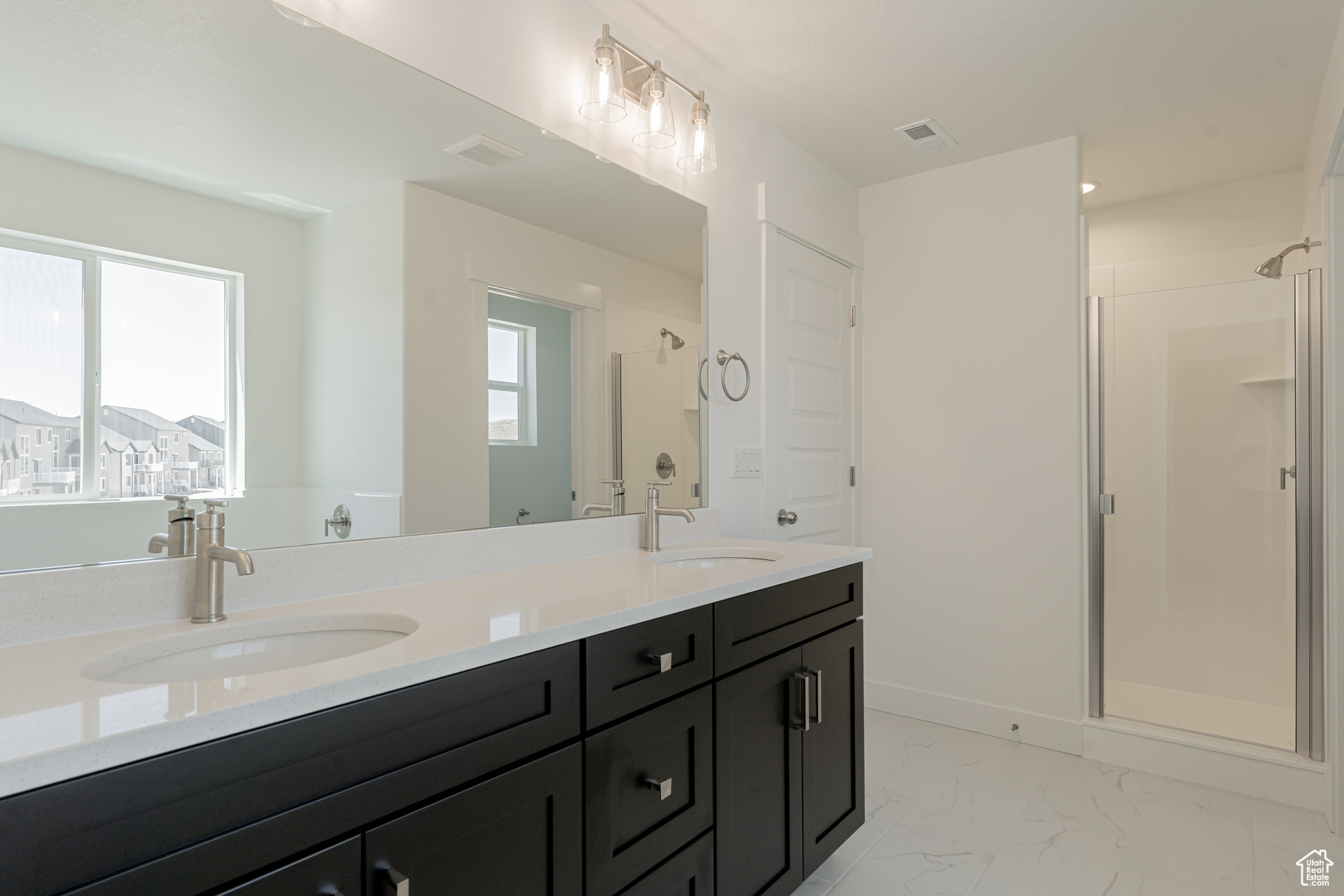 Bathroom featuring a healthy amount of sunlight, tile patterned floors, a shower with door, and dual bowl vanity