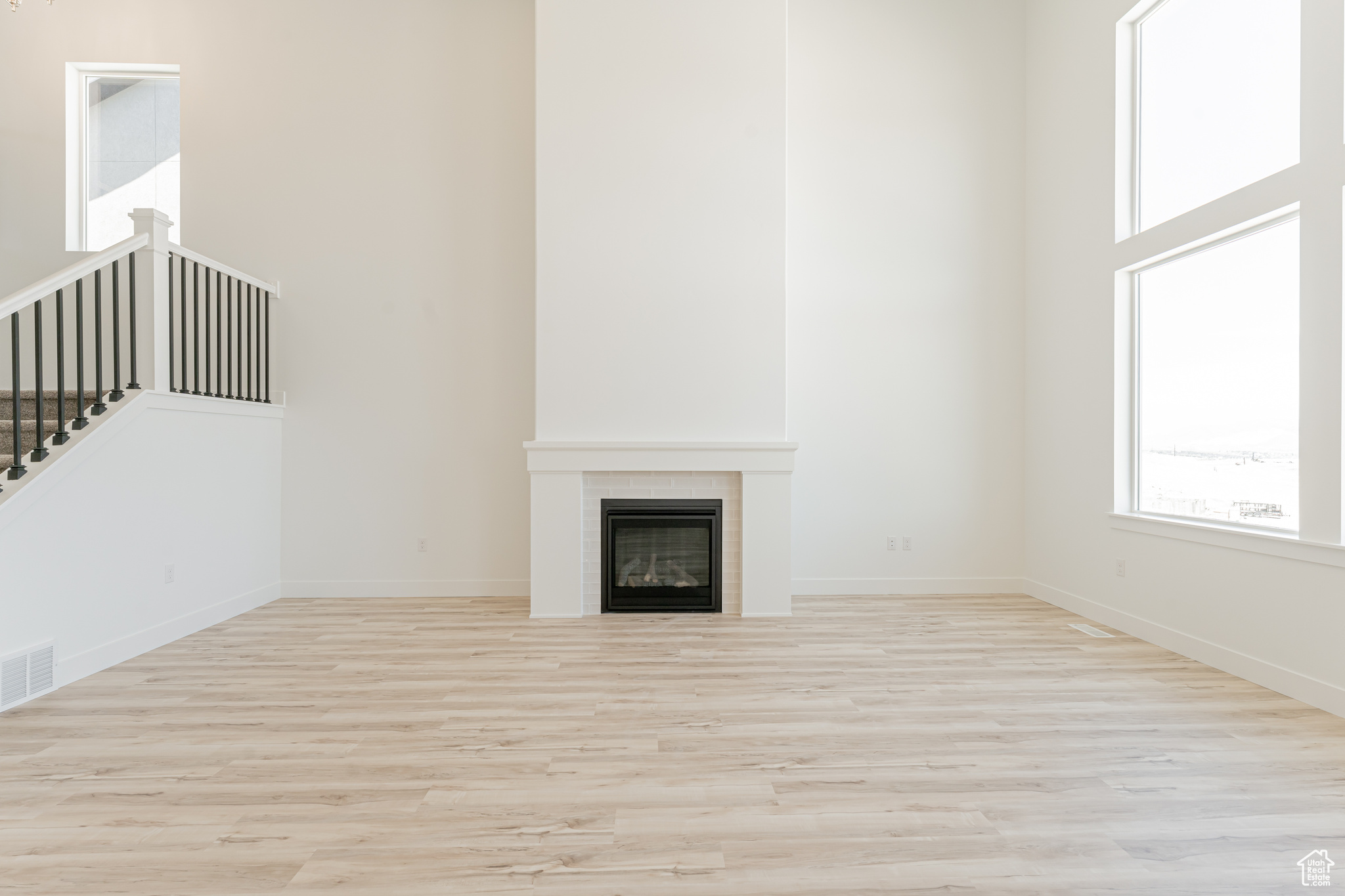 Unfurnished living room with a fireplace, light wood-type flooring, and a high ceiling