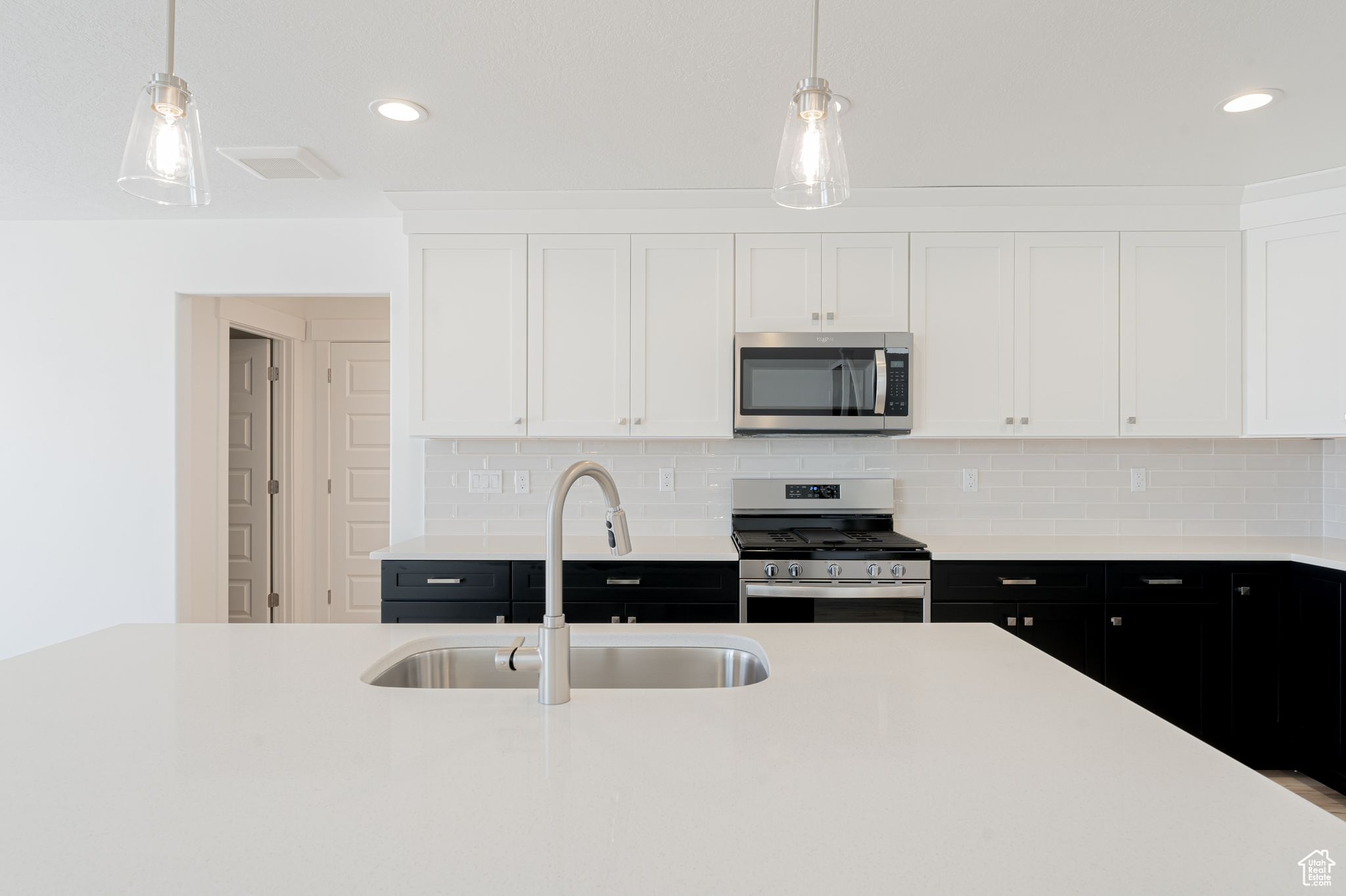 Kitchen featuring stainless steel appliances, sink, decorative light fixtures, decorative backsplash, and white cabinetry