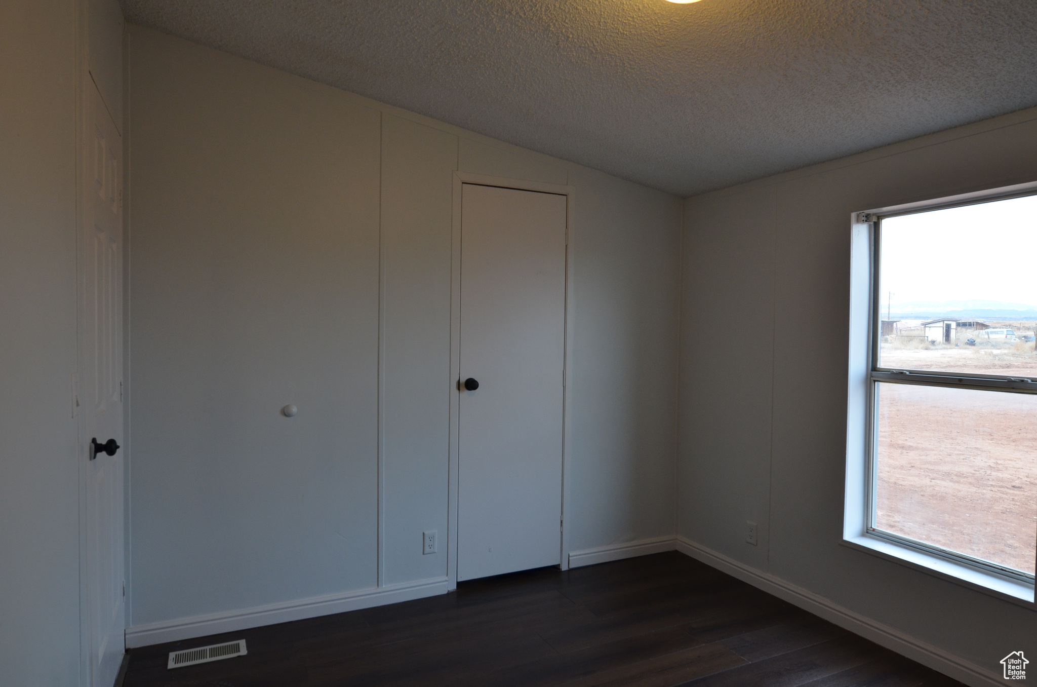 Unfurnished bedroom featuring a textured ceiling, lofted ceiling, a closet, and dark wood-type flooring