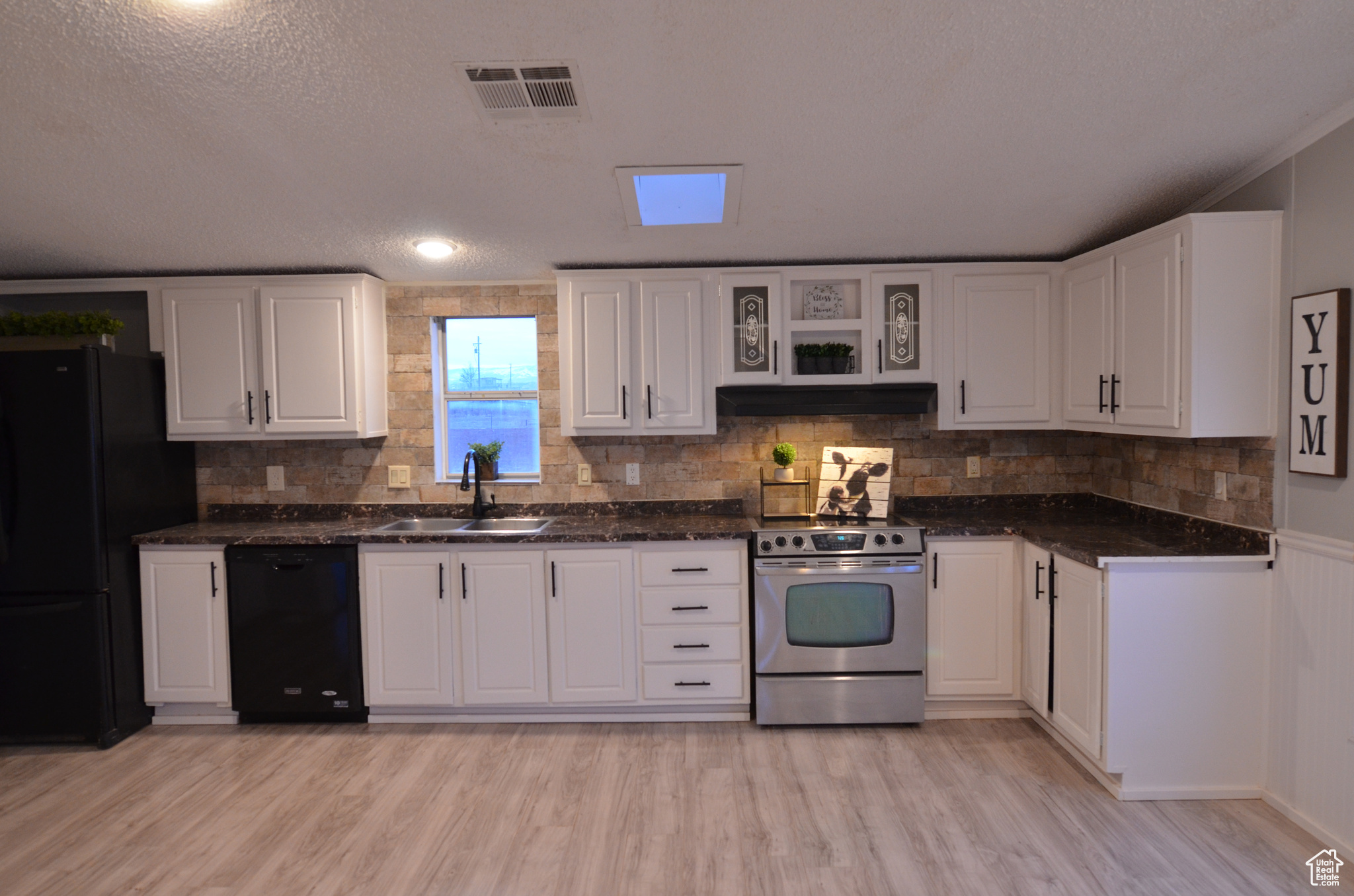 Kitchen featuring black appliances, sink, laminate flooring, and white cabinetry