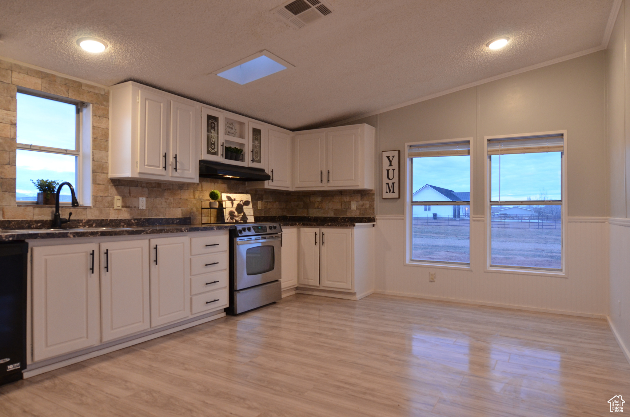 Kitchen featuring ornamental molding, white cabinetry, sink, light laminate flooring, and electric range