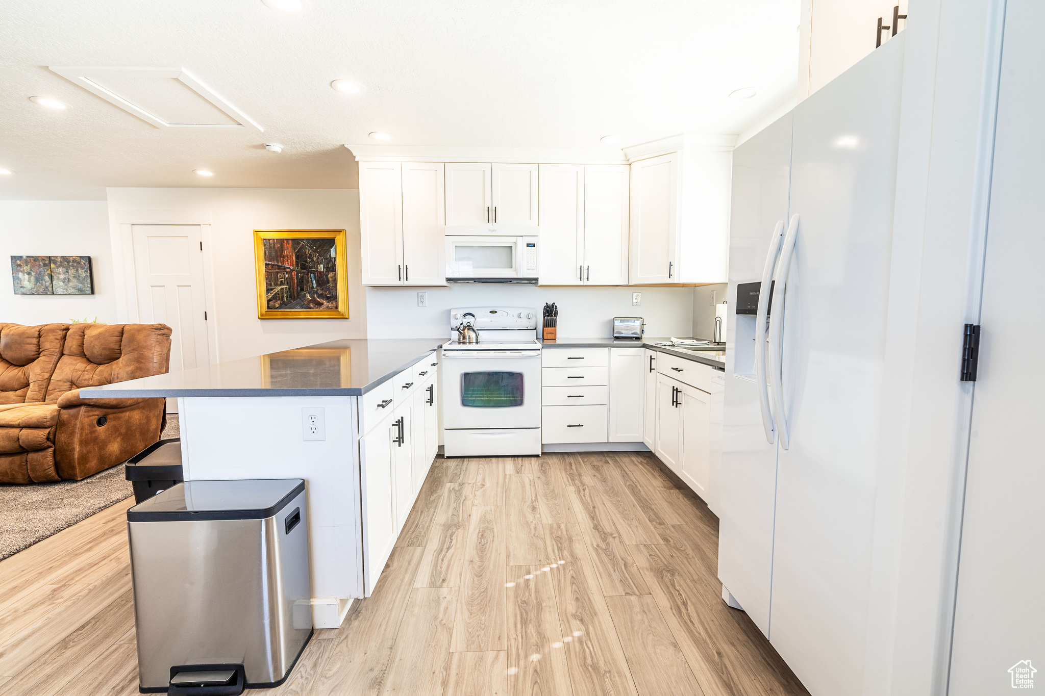 ADU kitchen with white cabinetry, white appliances, a breakfast bar area, and light hardwood / wood-style flooring