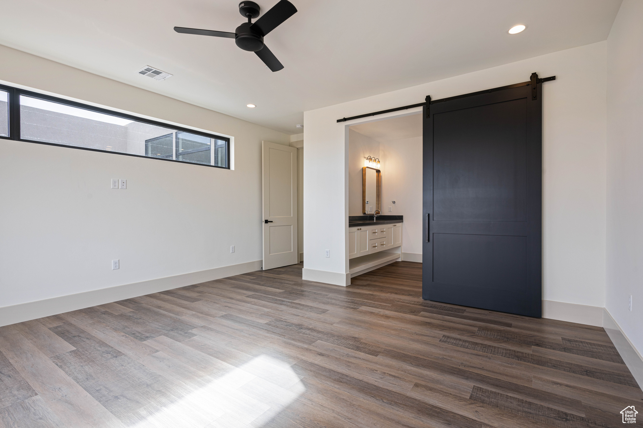 Unfurnished bedroom with dark hardwood / wood-style flooring, a barn door, ensuite bathroom, and ceiling fan