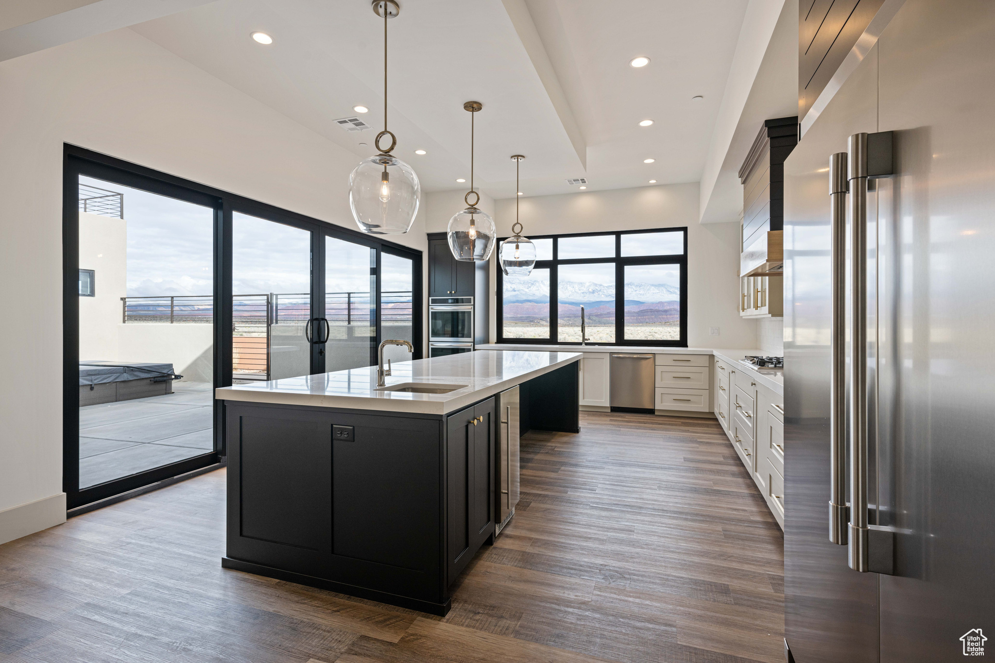 Kitchen with hardwood / wood-style flooring, white cabinets, stainless steel appliances, a kitchen island with sink, and decorative light fixtures