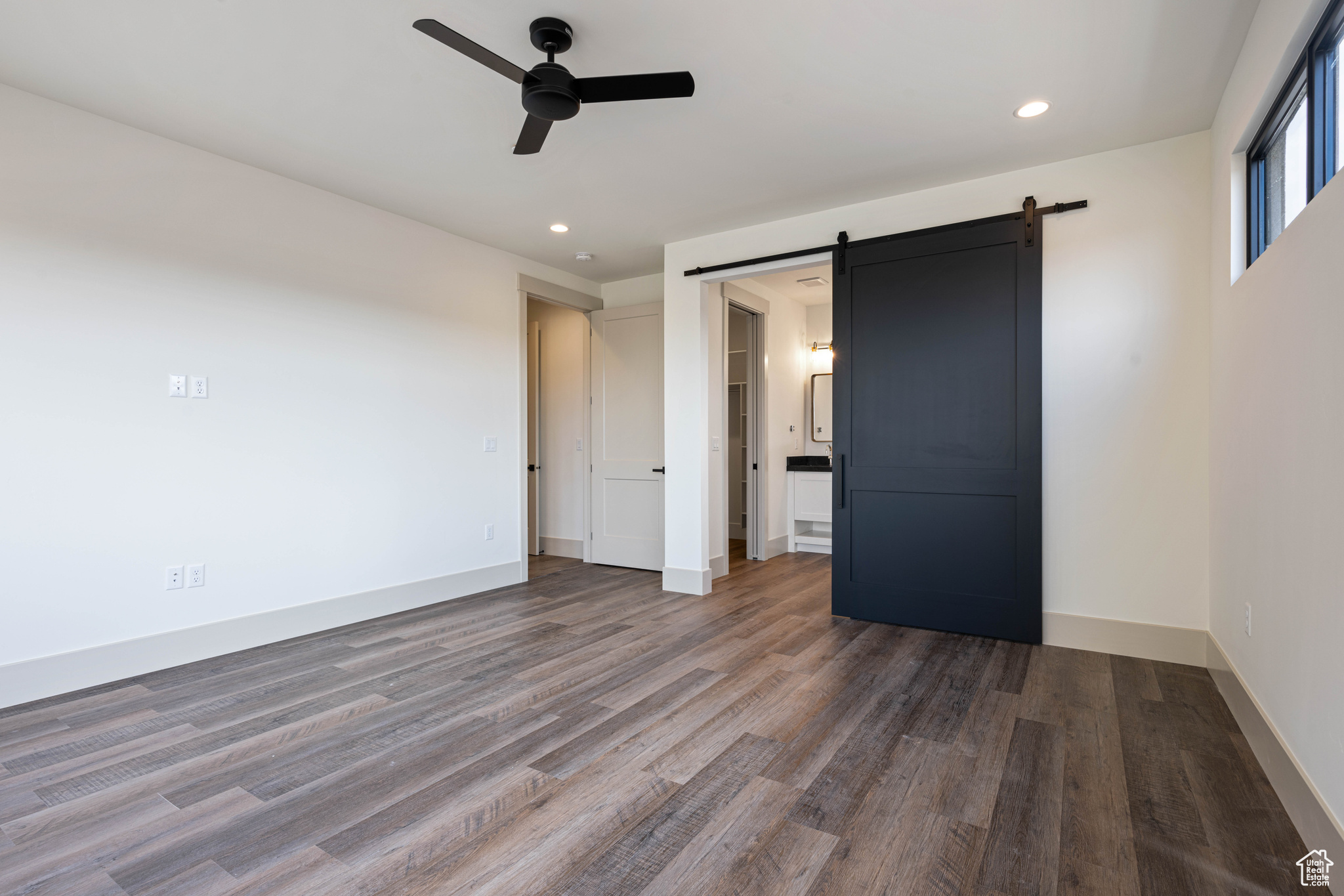 Spare room with ceiling fan, dark hardwood / wood-style floors, and a barn door