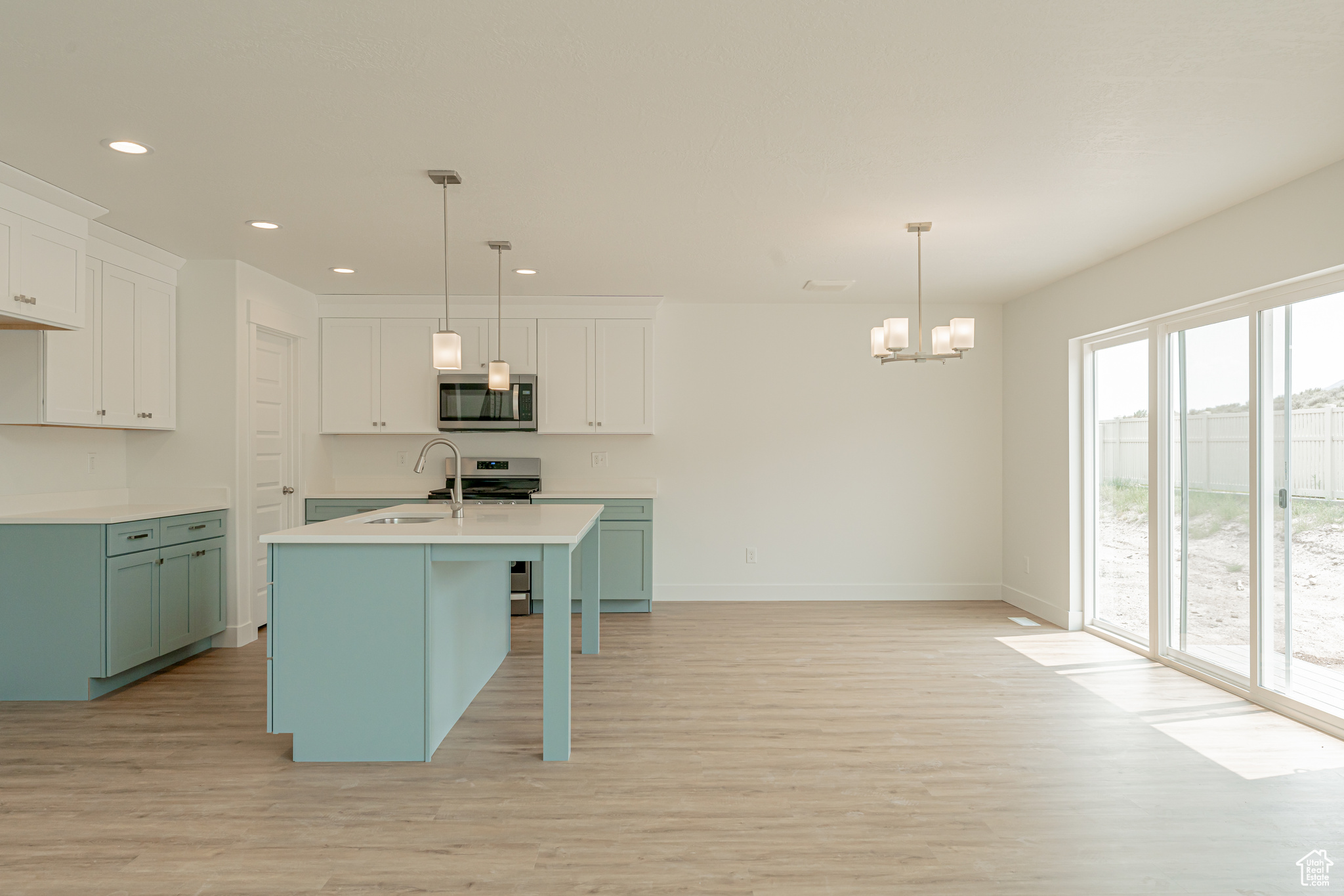 Kitchen with light wood-type flooring, white cabinets, a kitchen island with sink, stainless steel appliances, and decorative light fixtures