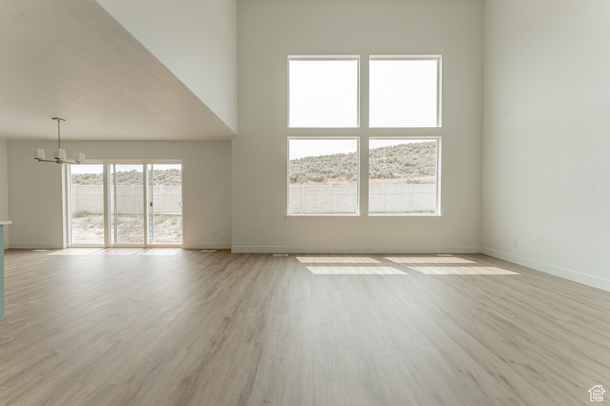 Spare room with a chandelier, light wood-type flooring, a towering ceiling, and a wealth of natural light