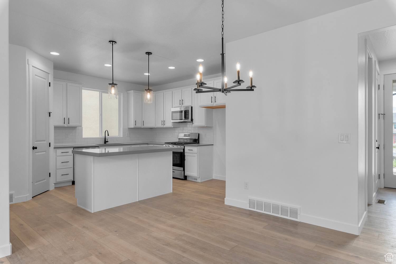 Kitchen with decorative backsplash, appliances with stainless steel finishes, light hardwood / wood-style flooring, and white cabinets