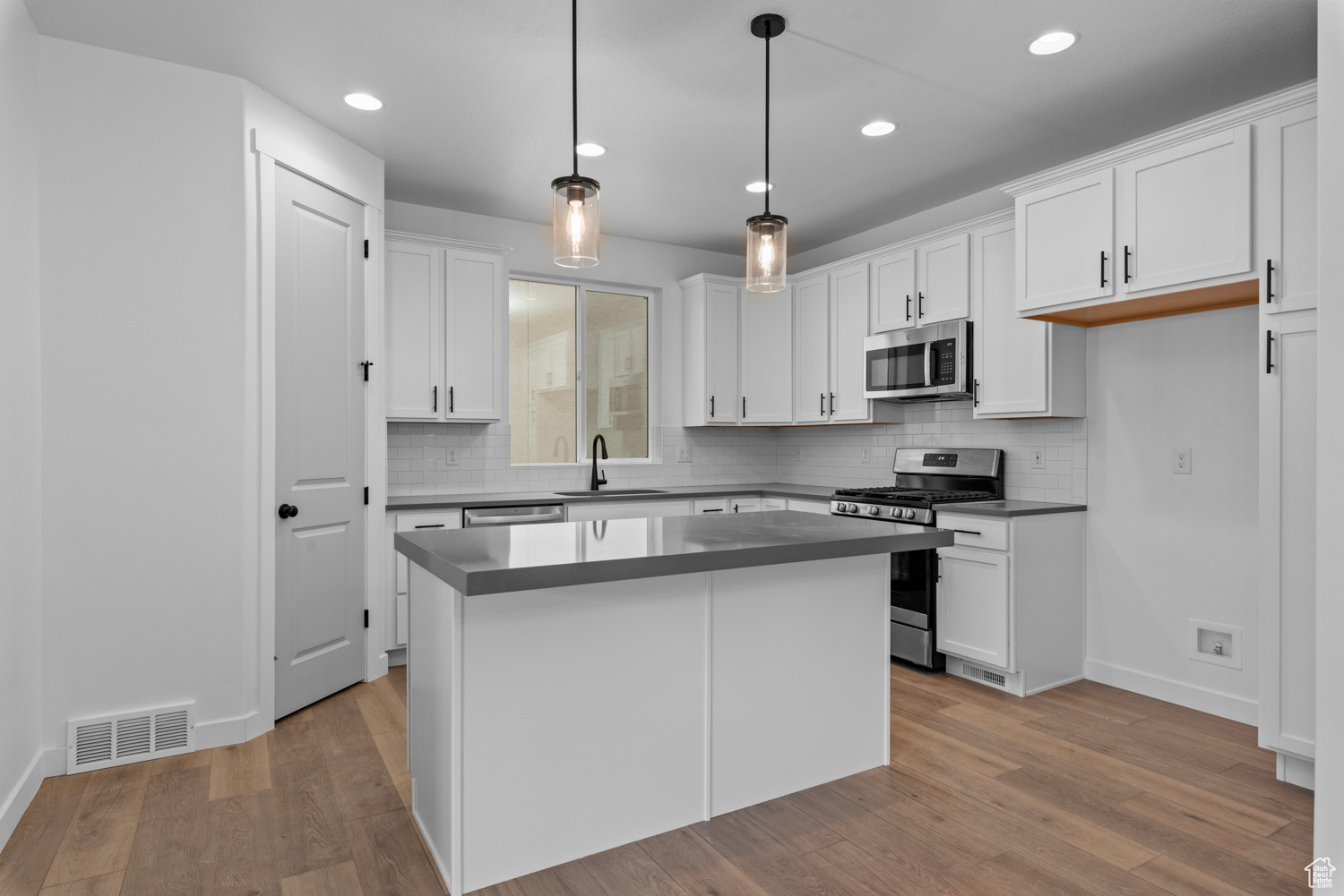 Kitchen featuring white cabinetry, light hardwood / wood-style flooring, appliances with stainless steel finishes, decorative light fixtures, and sink