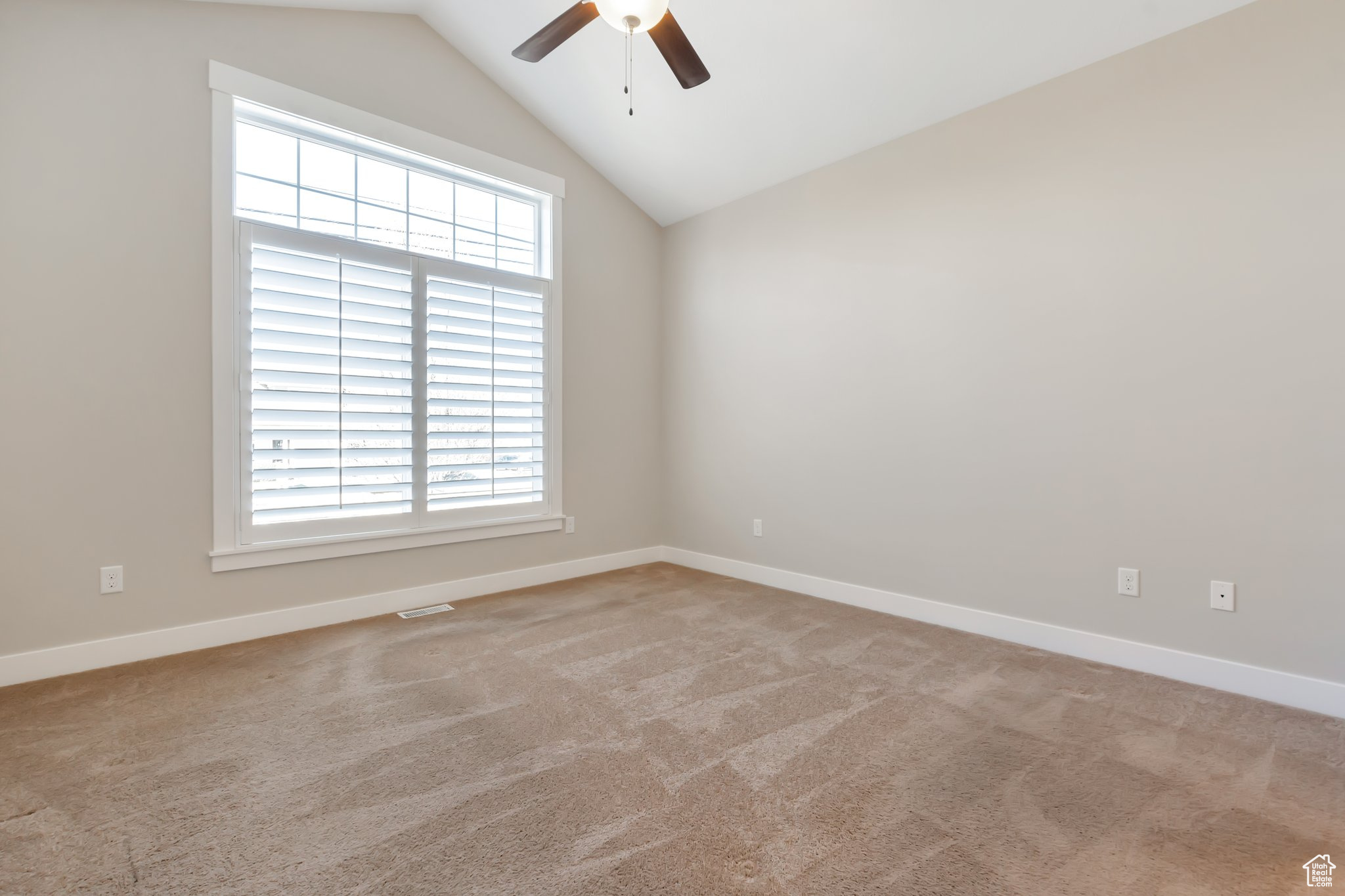 Empty room featuring vaulted ceiling, light colored carpet, a wealth of natural light, and ceiling fan
