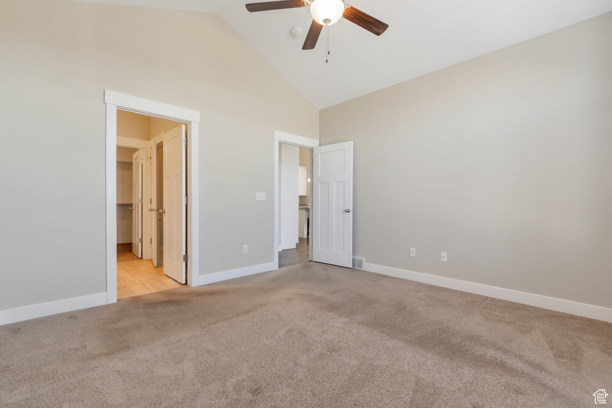 Unfurnished bedroom with high vaulted ceiling, light carpet, ceiling fan, and a walk in closet