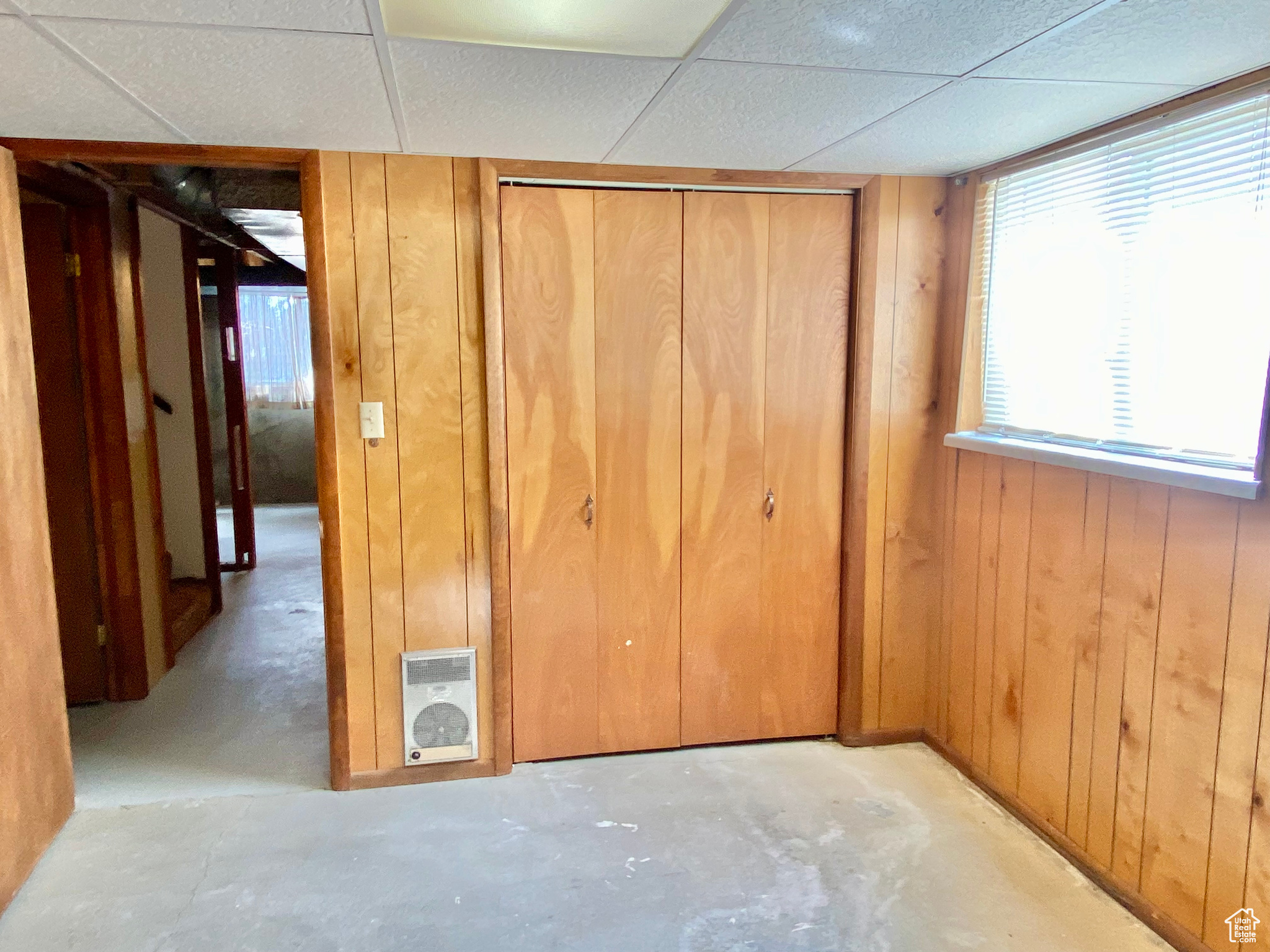 Unfurnished bedroom with wood walls, a closet, and a paneled ceiling