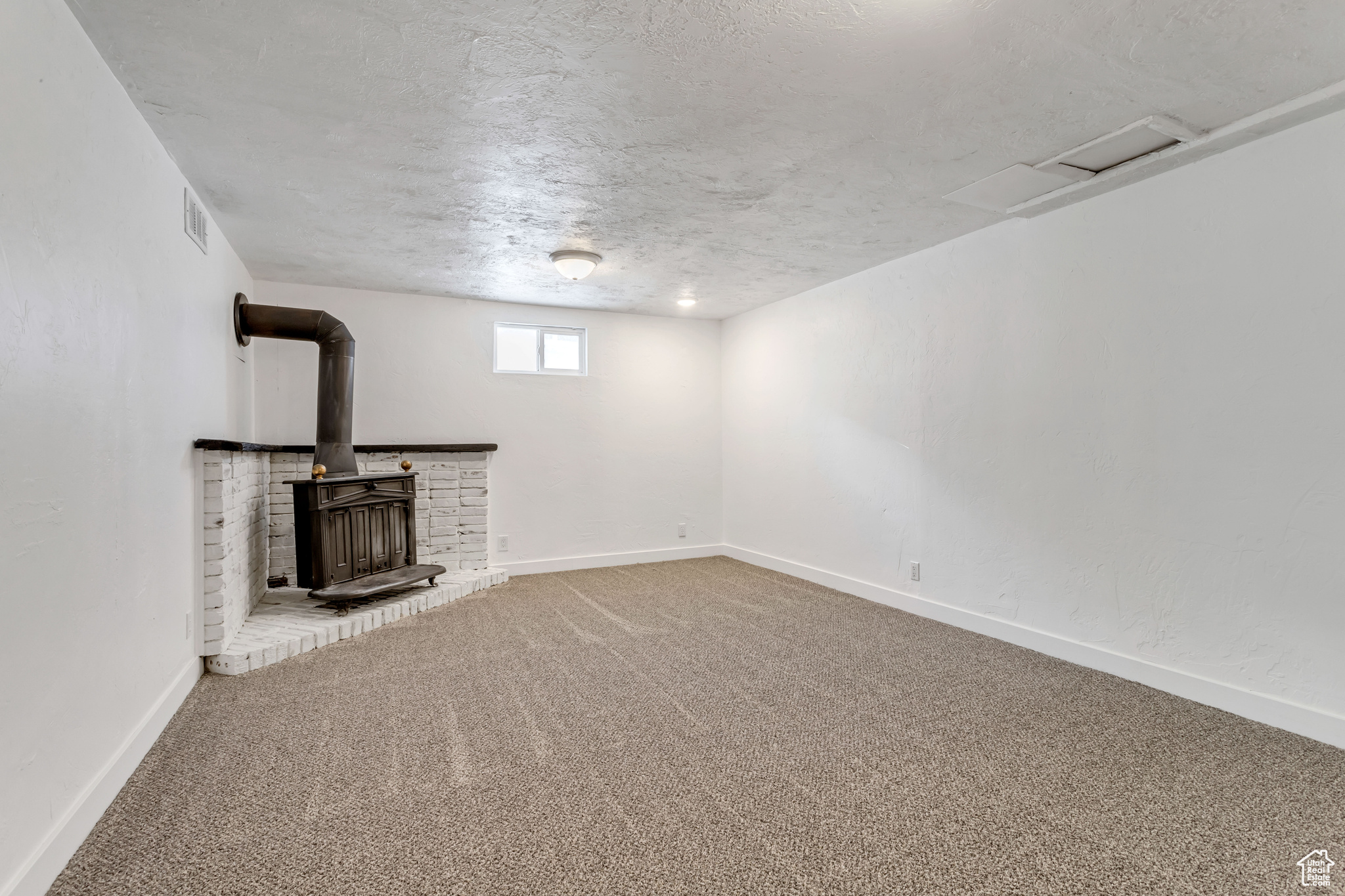Unfurnished living room with a wood stove, carpet floors, and a textured ceiling