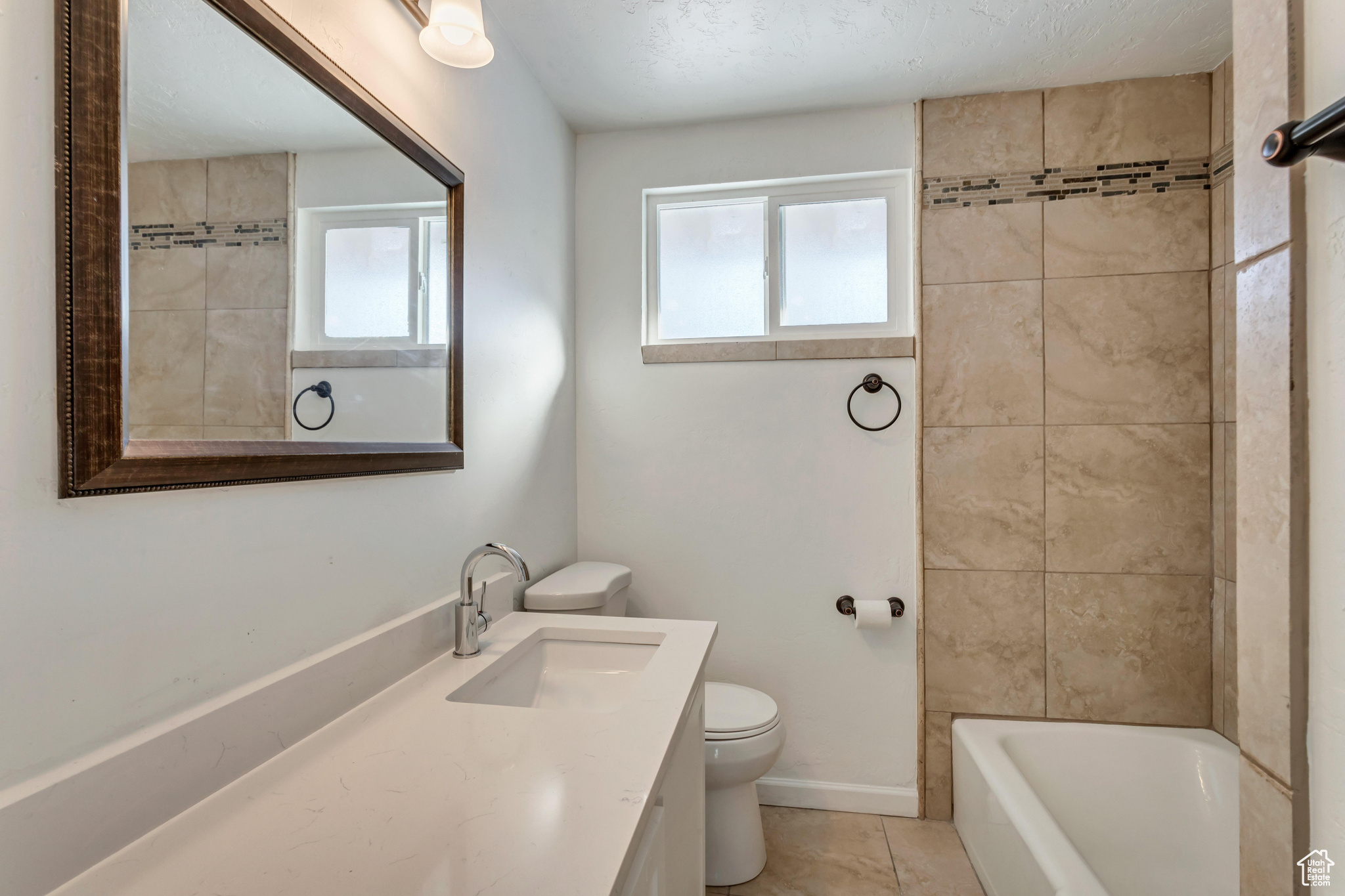 Full bathroom with tile flooring, tiled shower / bath, large vanity, and toilet