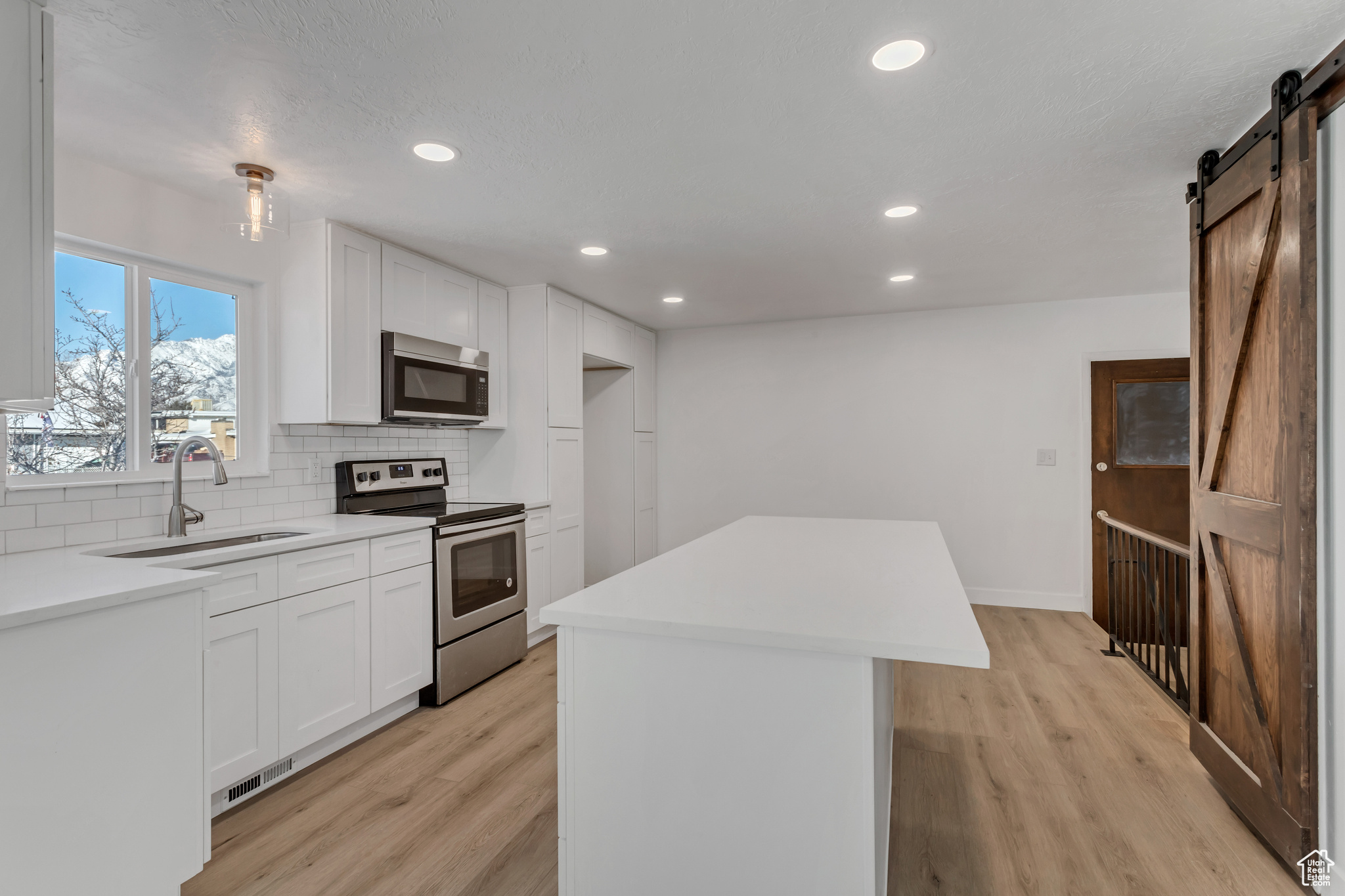 Kitchen with sink, stainless steel electric range, white cabinets, a barn door, and light hardwood / wood-style flooring