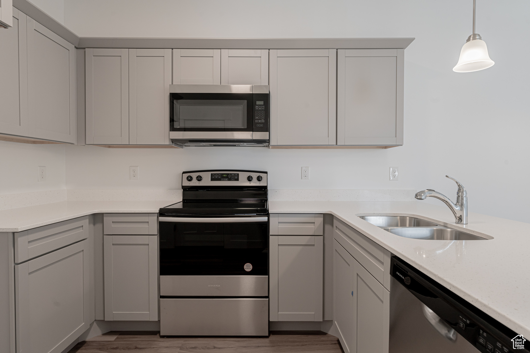 Kitchen with hardwood / wood-style flooring, gray cabinets, sink, decorative light fixtures, and stainless steel appliances