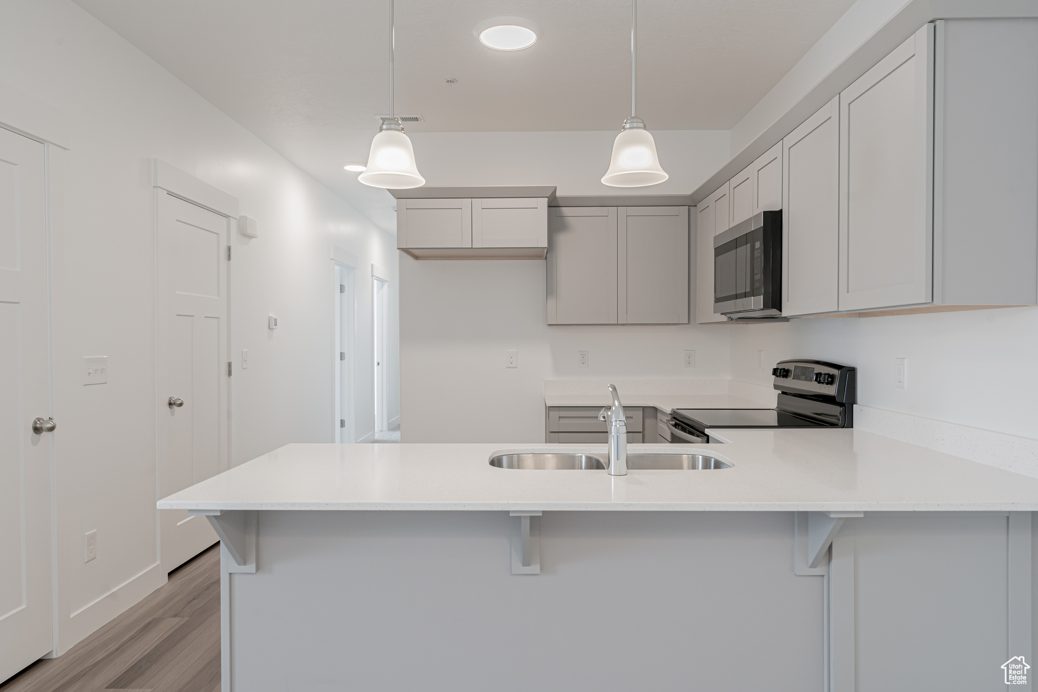 Kitchen featuring light hardwood / wood-style flooring, pendant lighting, appliances with stainless steel finishes, sink, and a breakfast bar area