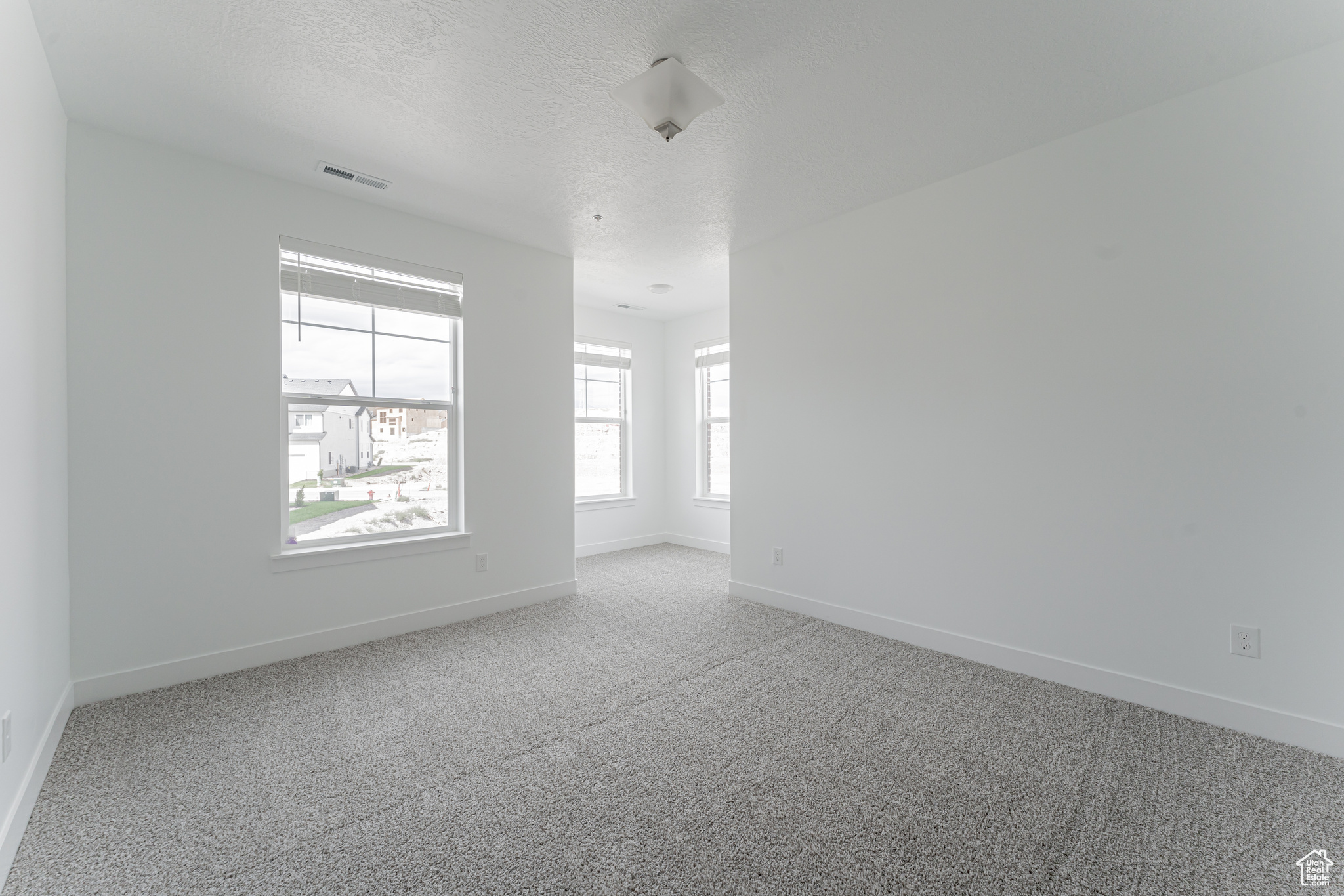 Empty room featuring light colored carpet and a textured ceiling