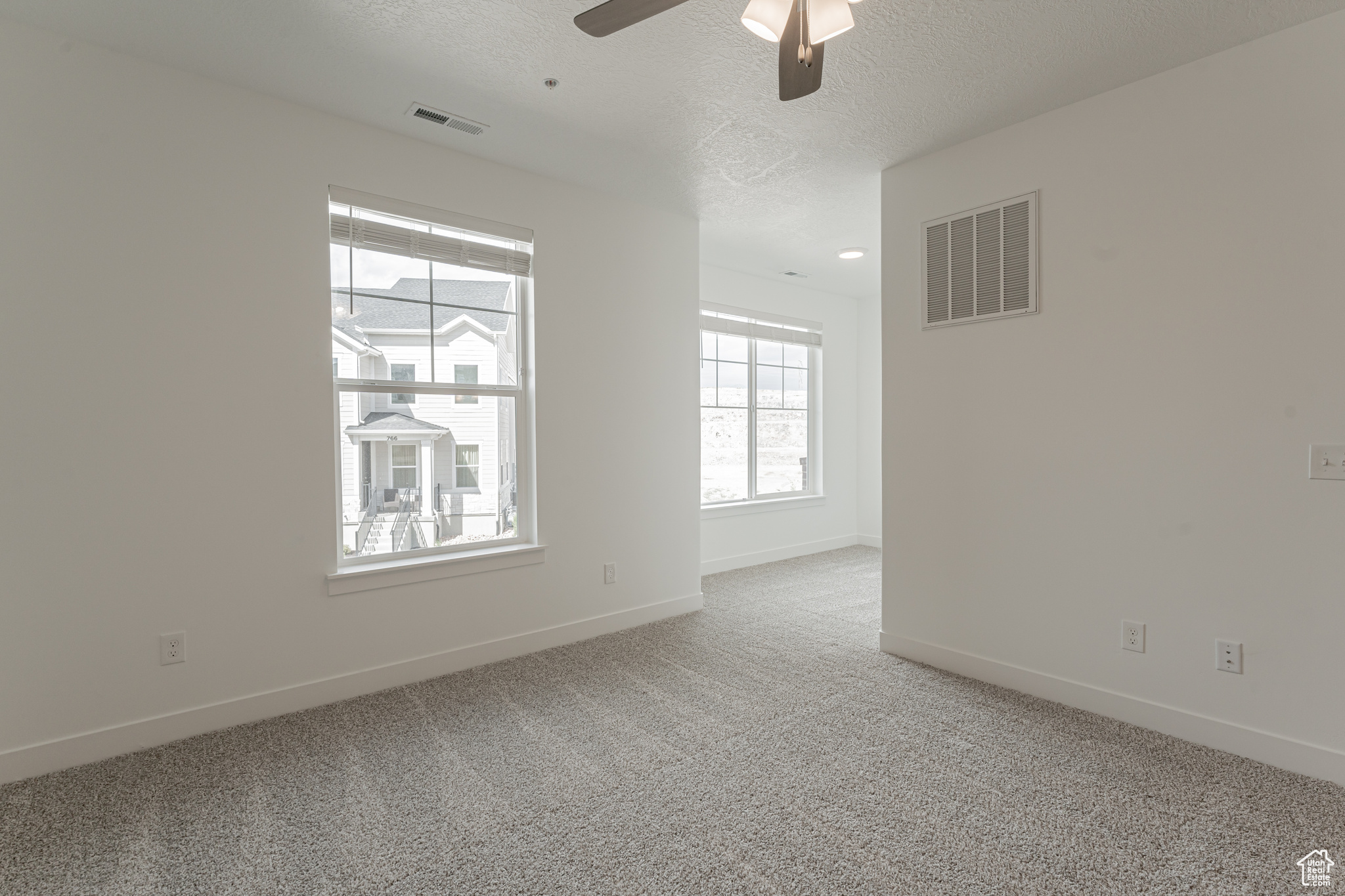 Carpeted empty room with a textured ceiling and ceiling fan