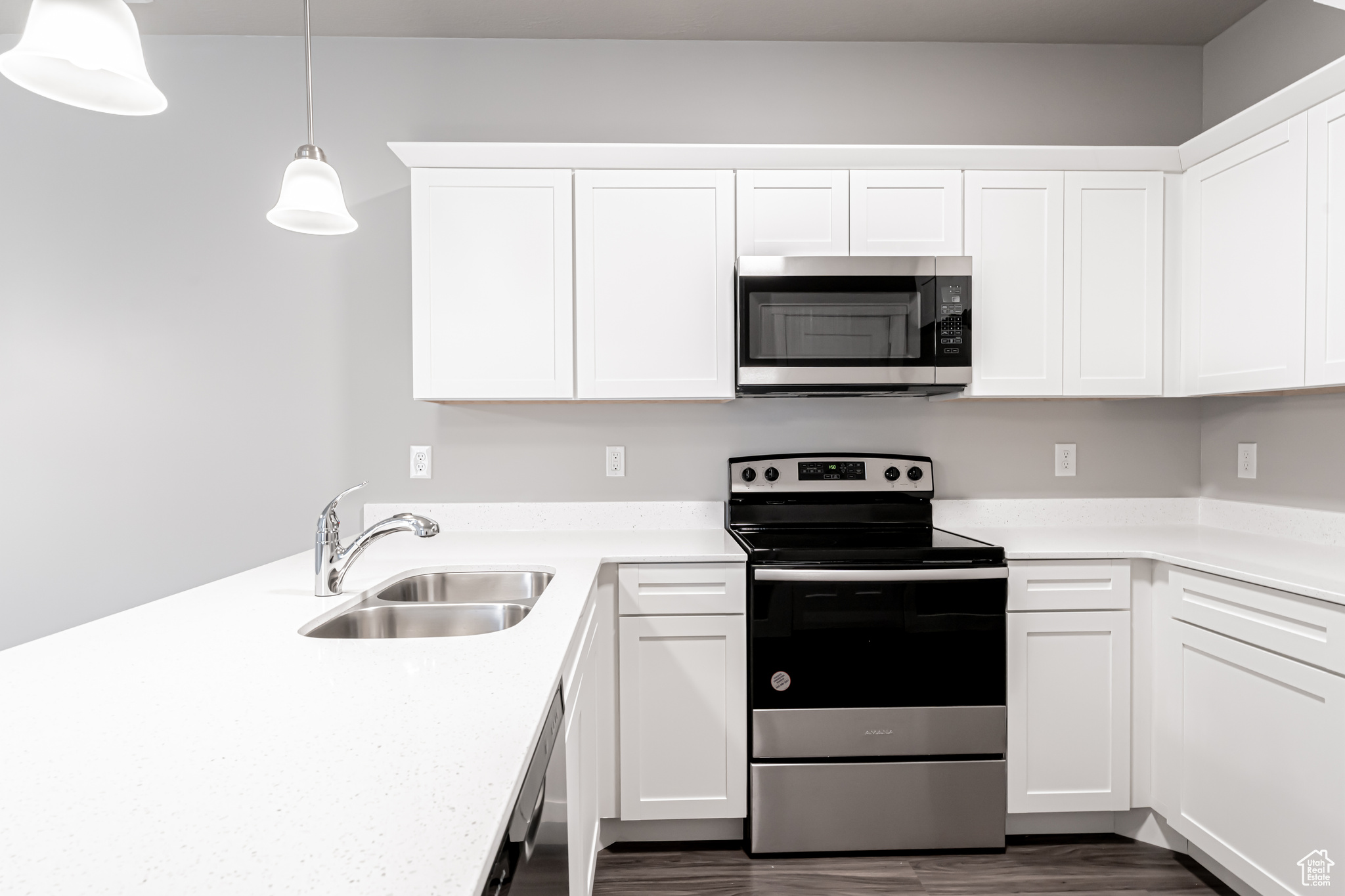 Kitchen with dark wood-type flooring, sink, pendant lighting, white cabinetry, and appliances with stainless steel finishes