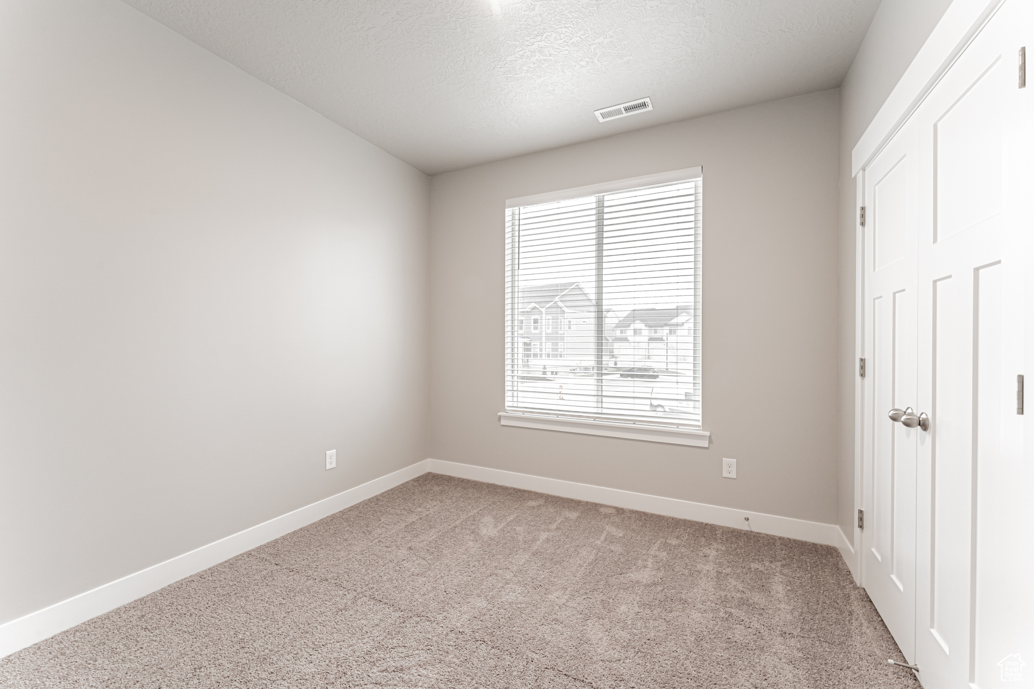 Unfurnished room with light carpet, a textured ceiling, and a healthy amount of sunlight