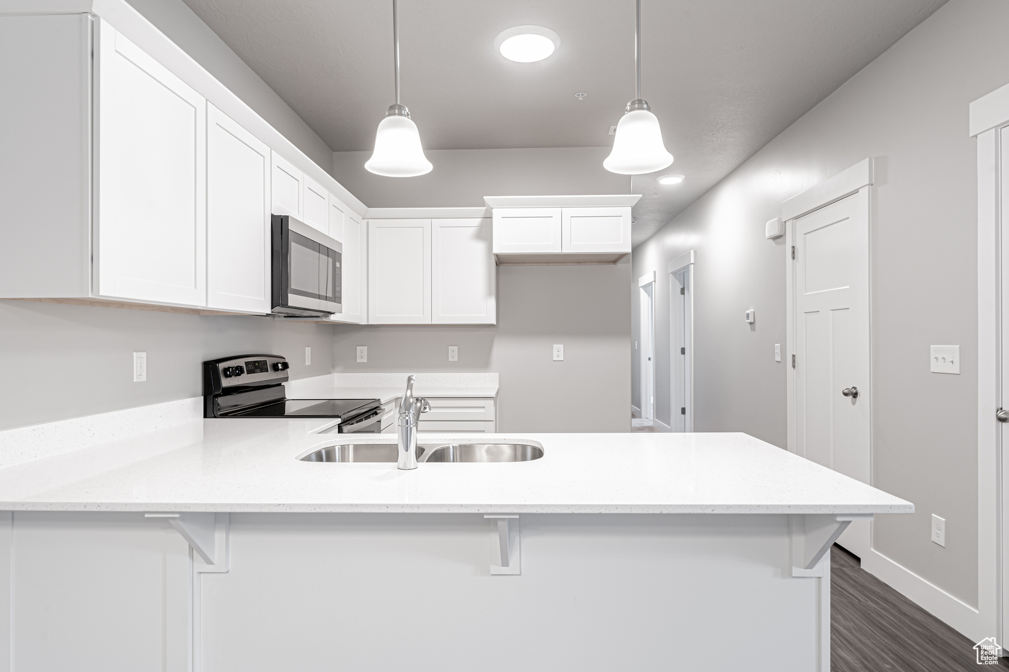 Kitchen with white cabinetry, electric stove, decorative light fixtures, and a breakfast bar