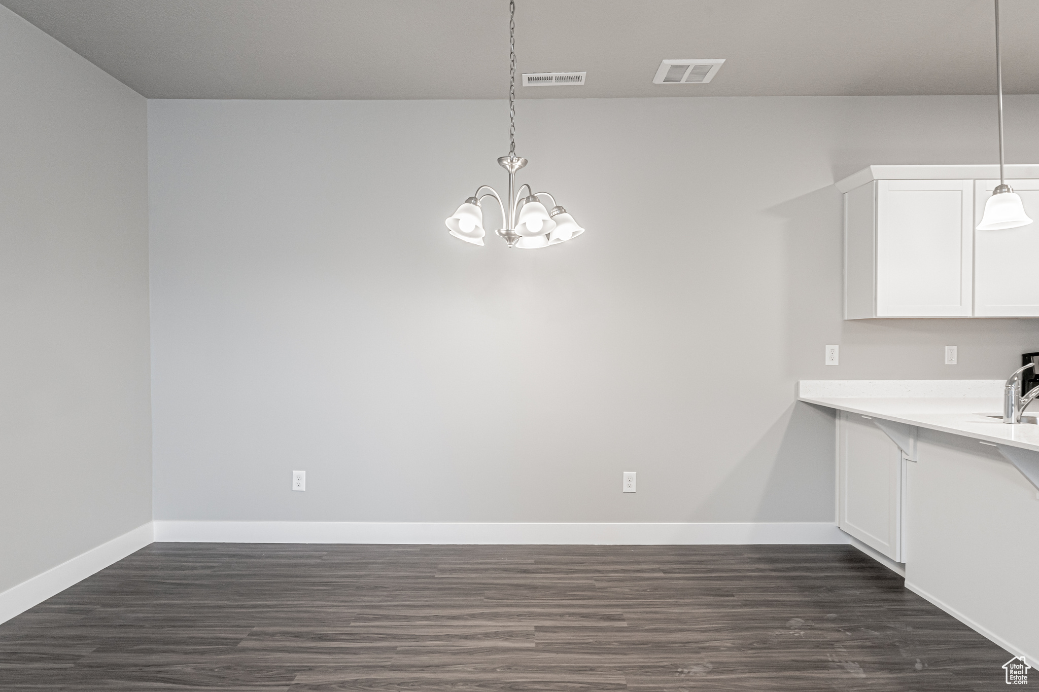 Unfurnished dining area with an inviting chandelier, sink, and dark hardwood / wood-style flooring