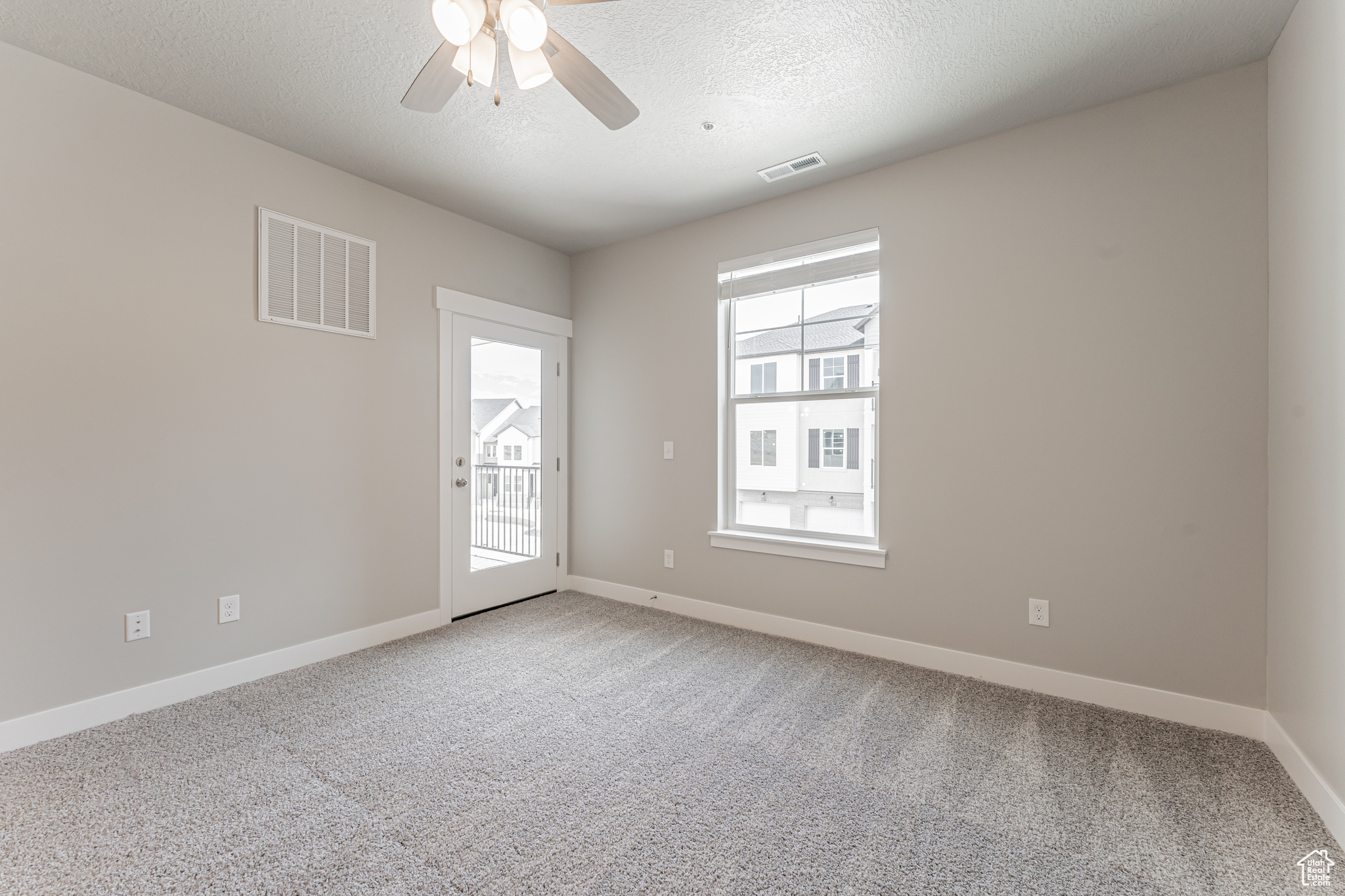 Empty room with light colored carpet, a textured ceiling, and ceiling fan