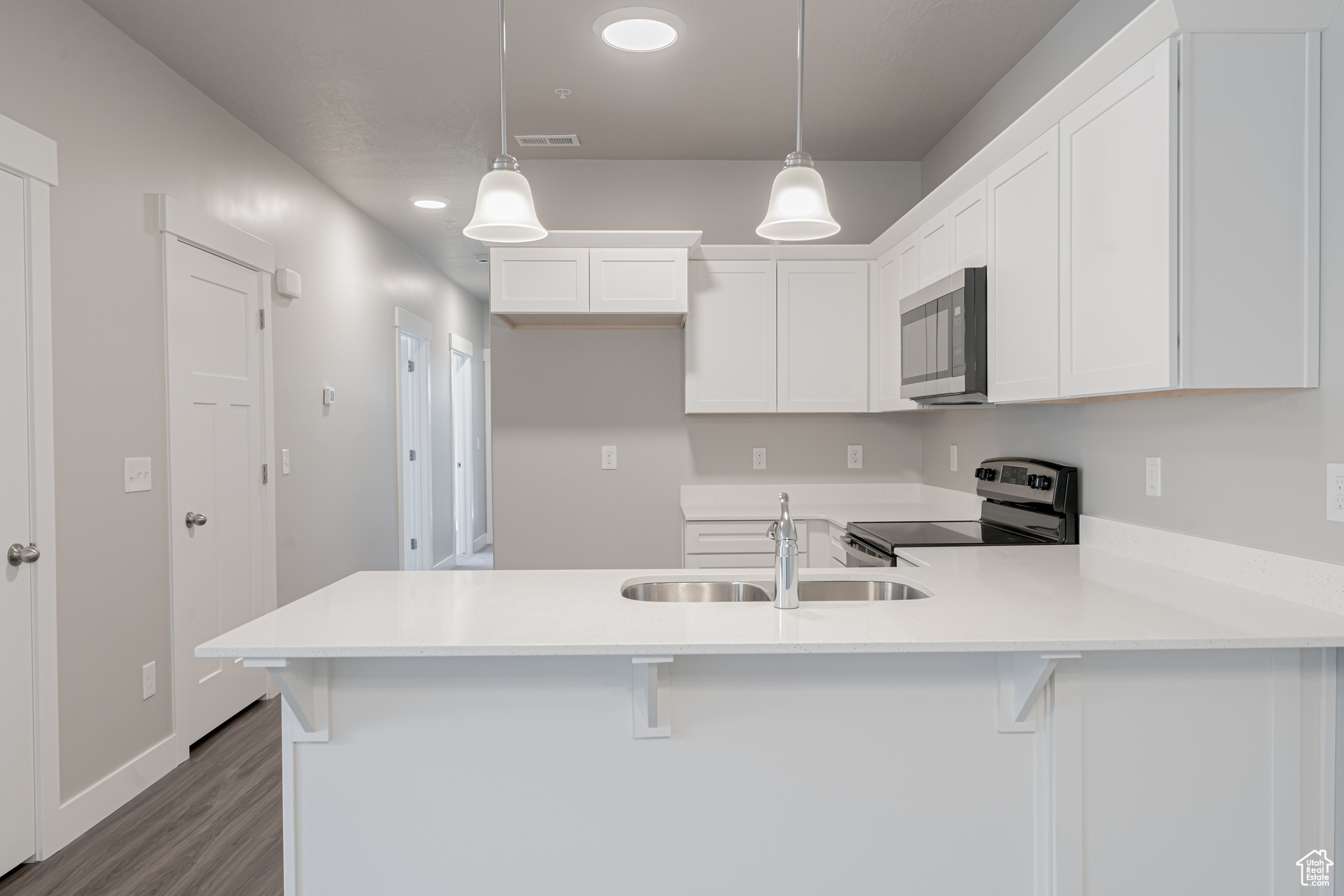 Kitchen with appliances with stainless steel finishes, decorative light fixtures, hardwood / wood-style floors, white cabinets, and kitchen peninsula