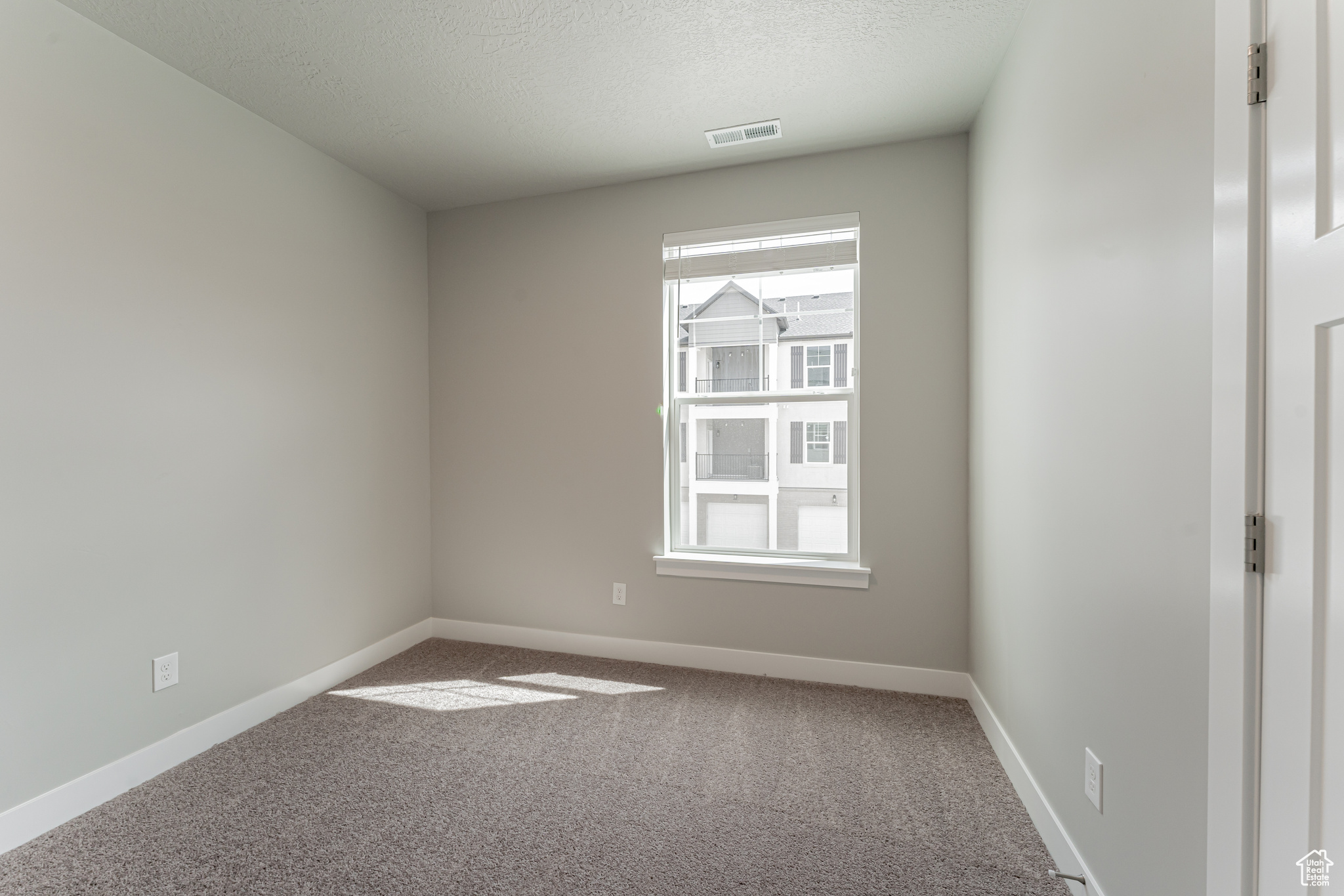 Carpeted spare room featuring a textured ceiling and a healthy amount of sunlight