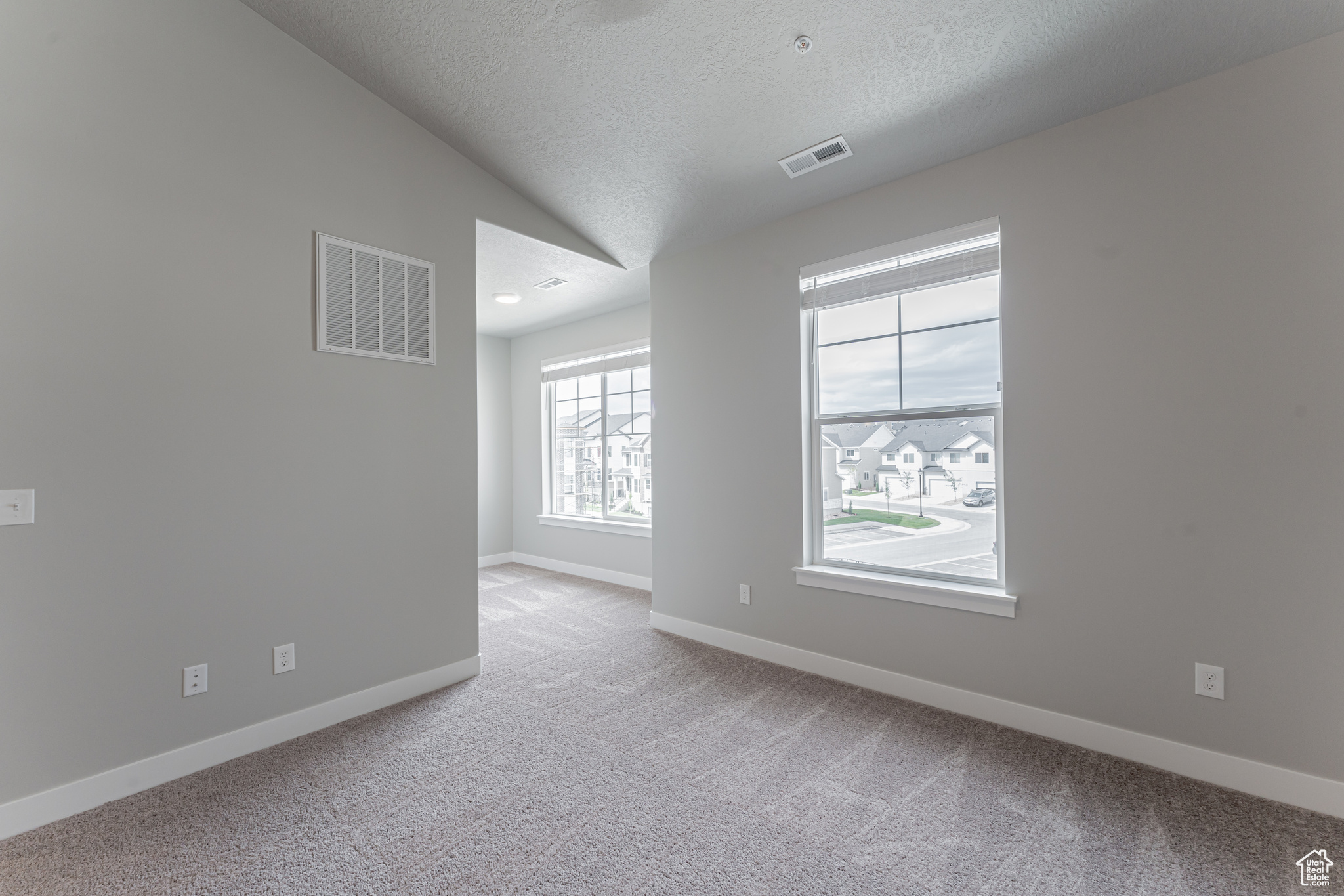 Carpeted empty room with a textured ceiling and lofted ceiling