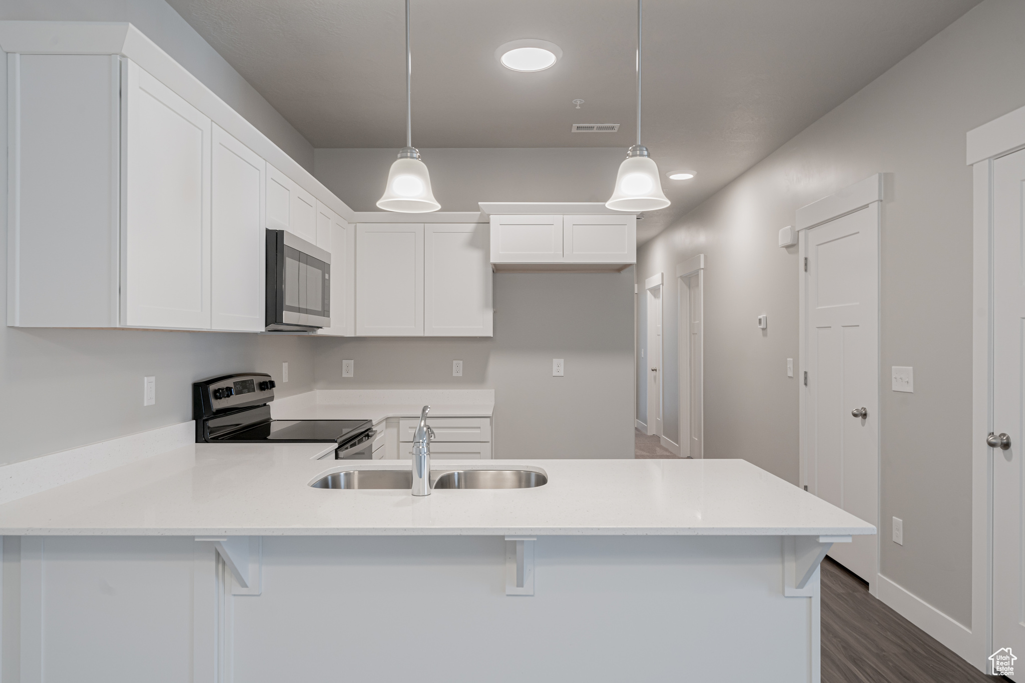 Kitchen featuring stainless steel appliances, white cabinetry, kitchen peninsula, dark wood-type flooring, and hanging light fixtures