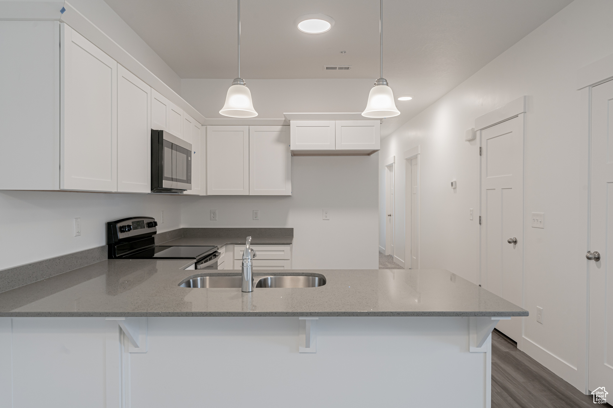 Kitchen with dark wood-type flooring, pendant lighting, white cabinets, kitchen peninsula, and stainless steel appliances