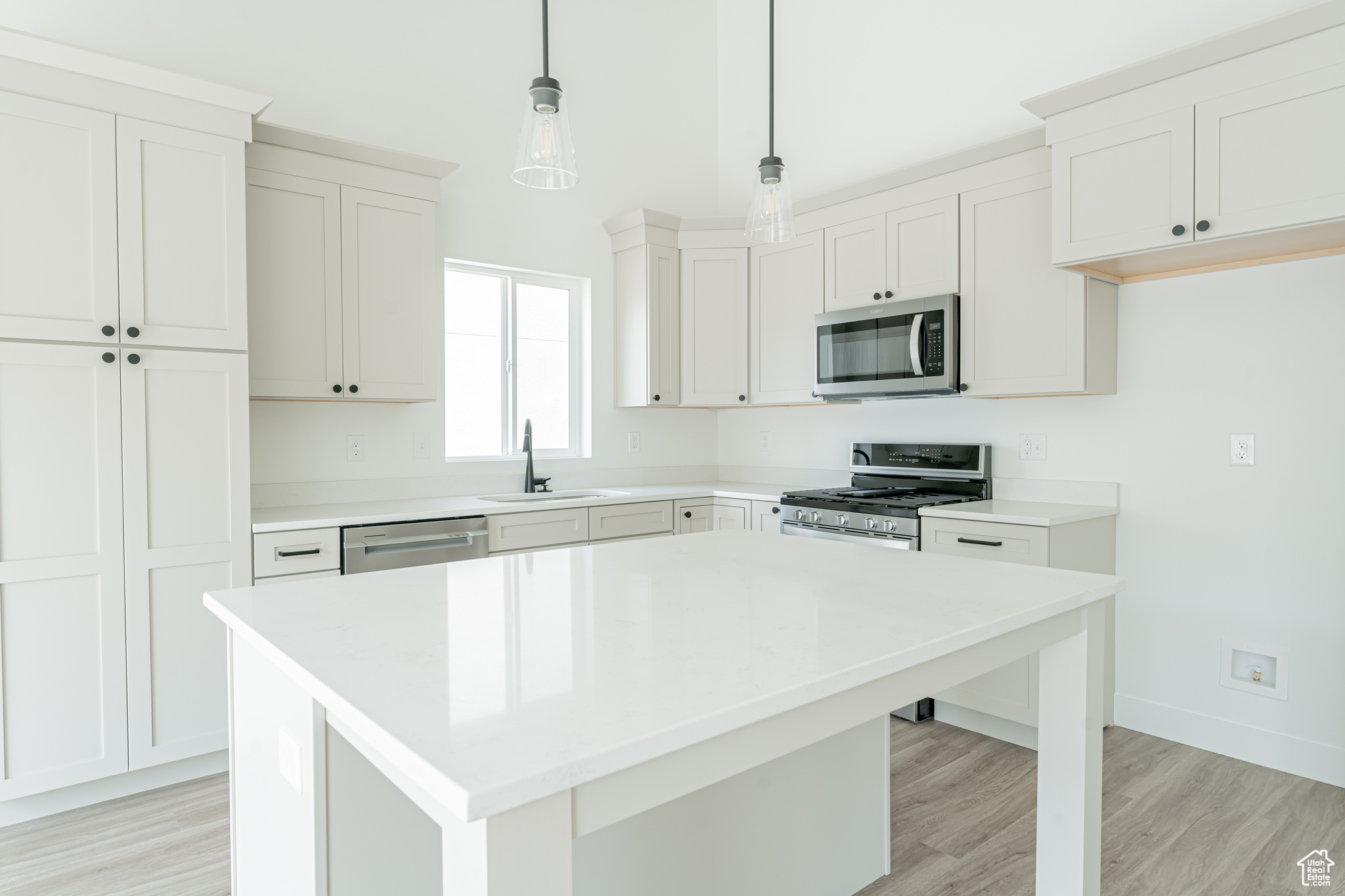 Kitchen with a center island, stainless steel appliances, light hardwood / wood-style floors, decorative light fixtures, and sink